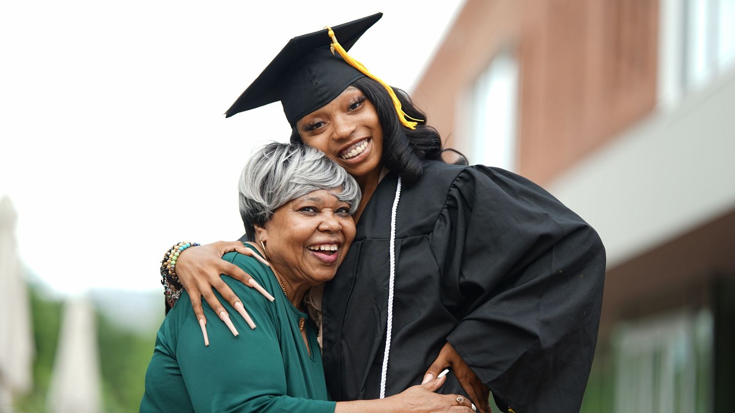 Graduate in cap and gown shares joyful moment with supporter outdoors.