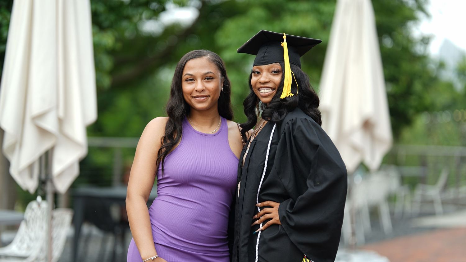Graduate in black cap and gown celebrates with supporters in purple attire.