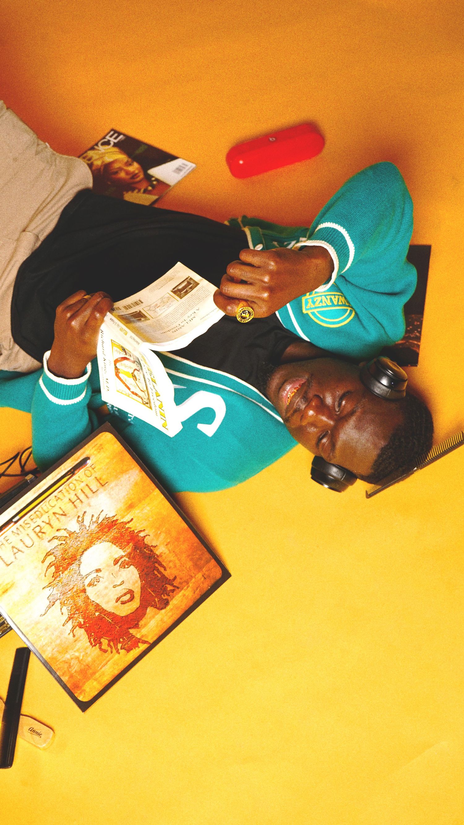 Person lying on orange background surrounded by books and media materials.