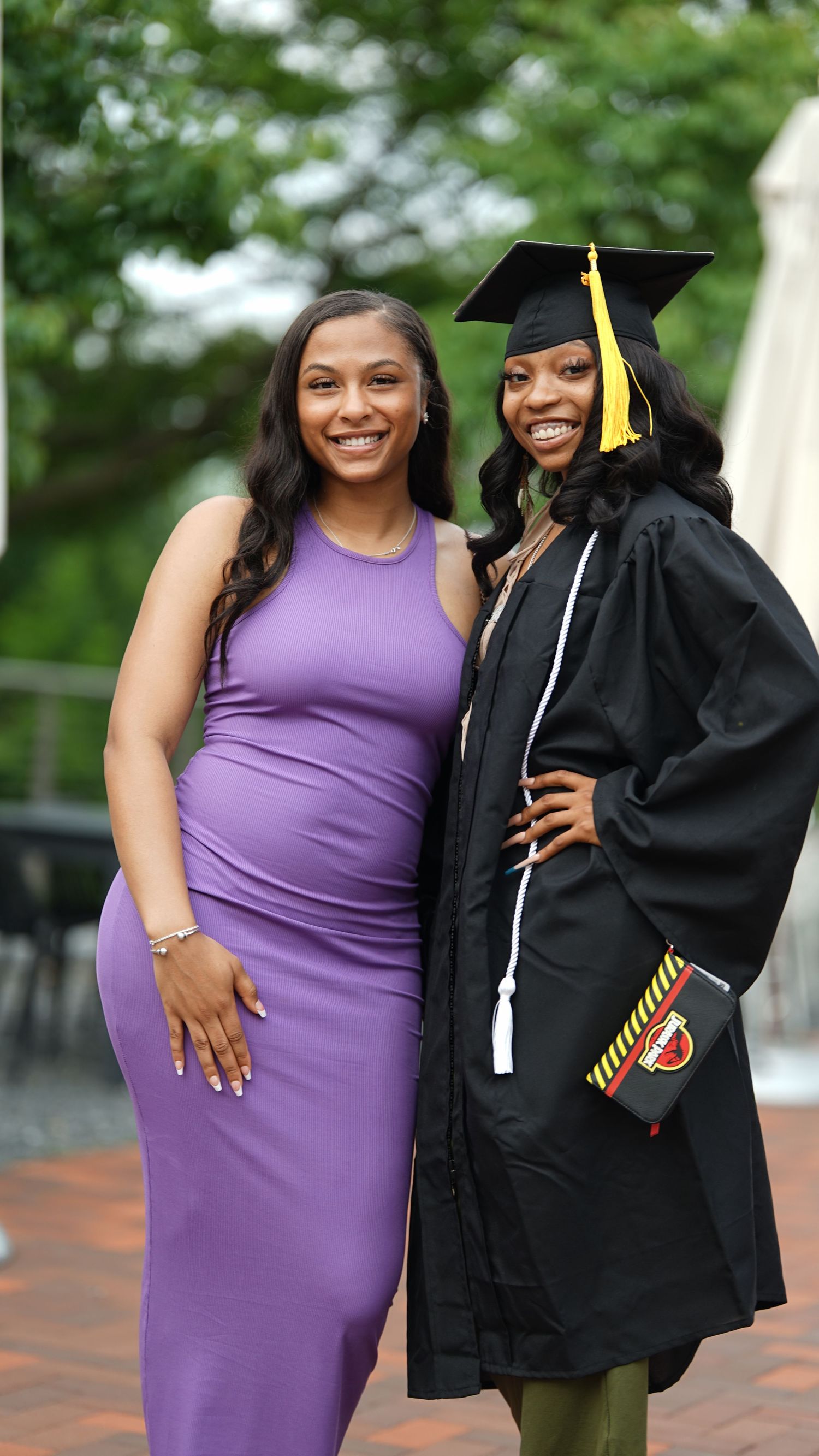 Two people share happy smiles during graduation photo session on brick courtyard.