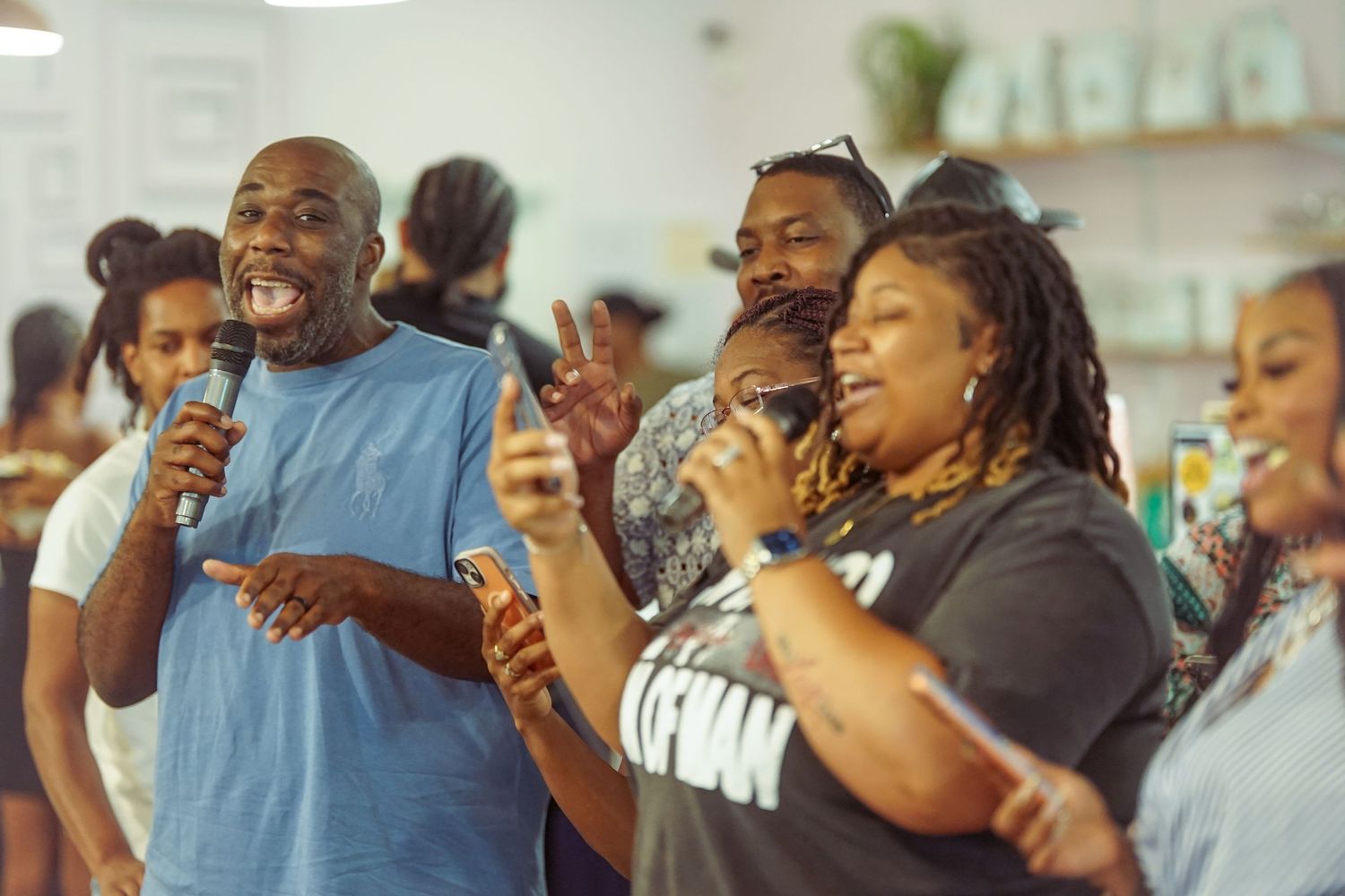 Group of people singing and dancing together at a lively indoor community event, holding microphones.