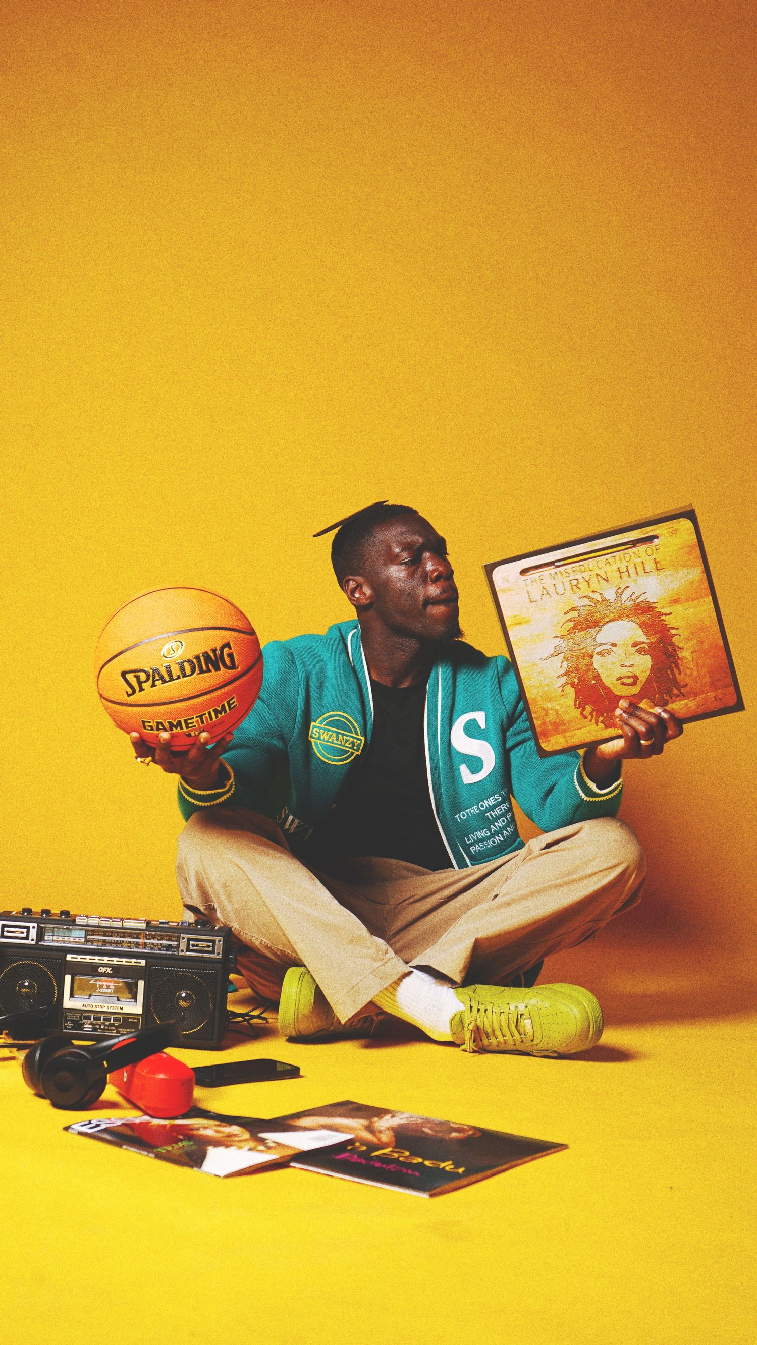 Person lying on yellow background with books and Spalding basketball.