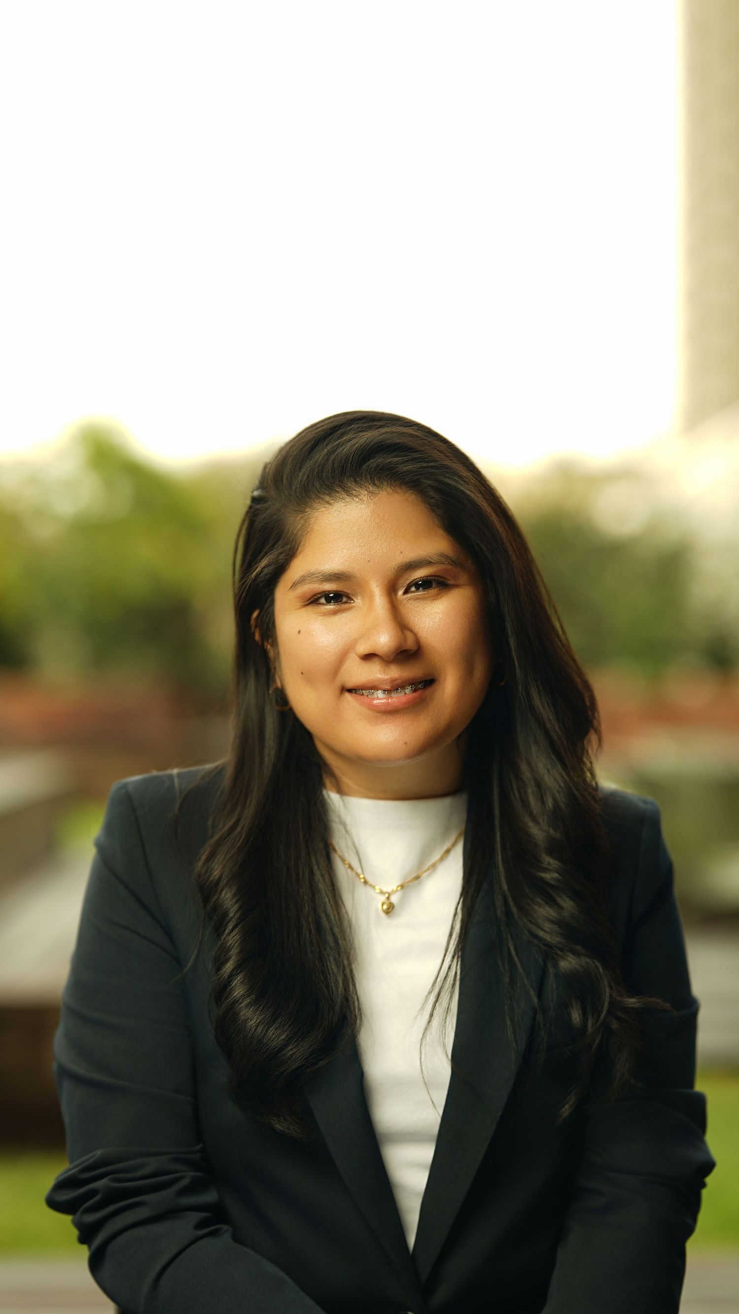 Professional headshots of someone in a black blazer and white top against a blurred outdoor setting.