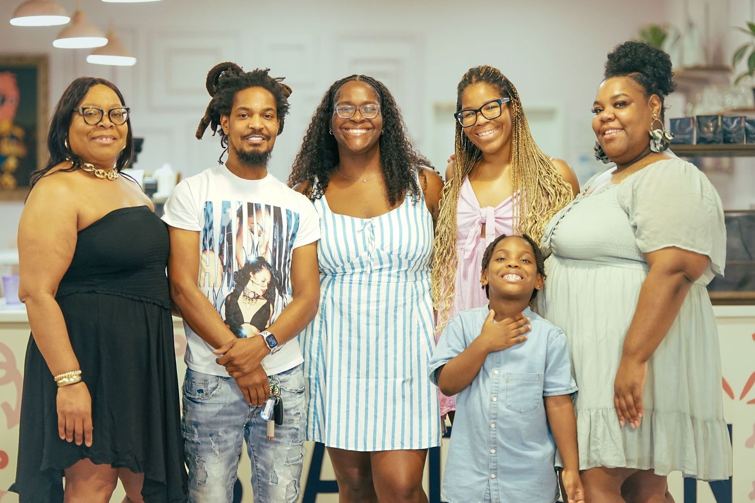Group of six adults and one child posing together indoors, smiling at a casual social gathering in a bright space.
