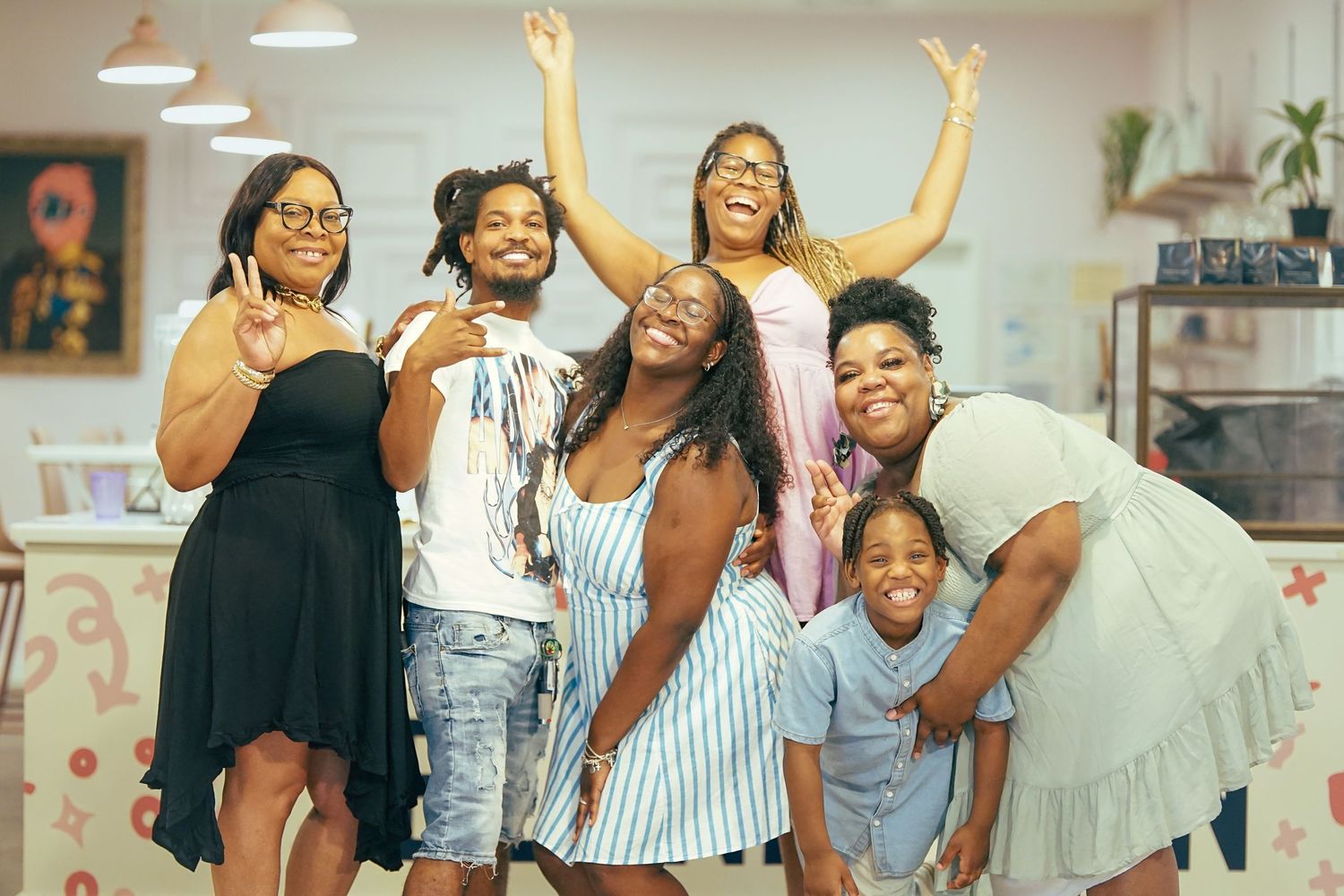 Group of joyful Black women and children posing and smiling together inside a bright, colorful cafe.