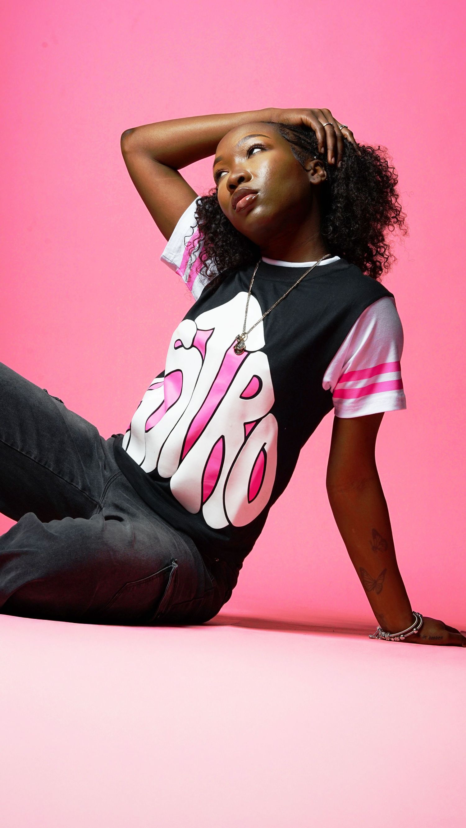 A fashion model wearing a black and pink graphic t-shirt poses against a vibrant pink background.