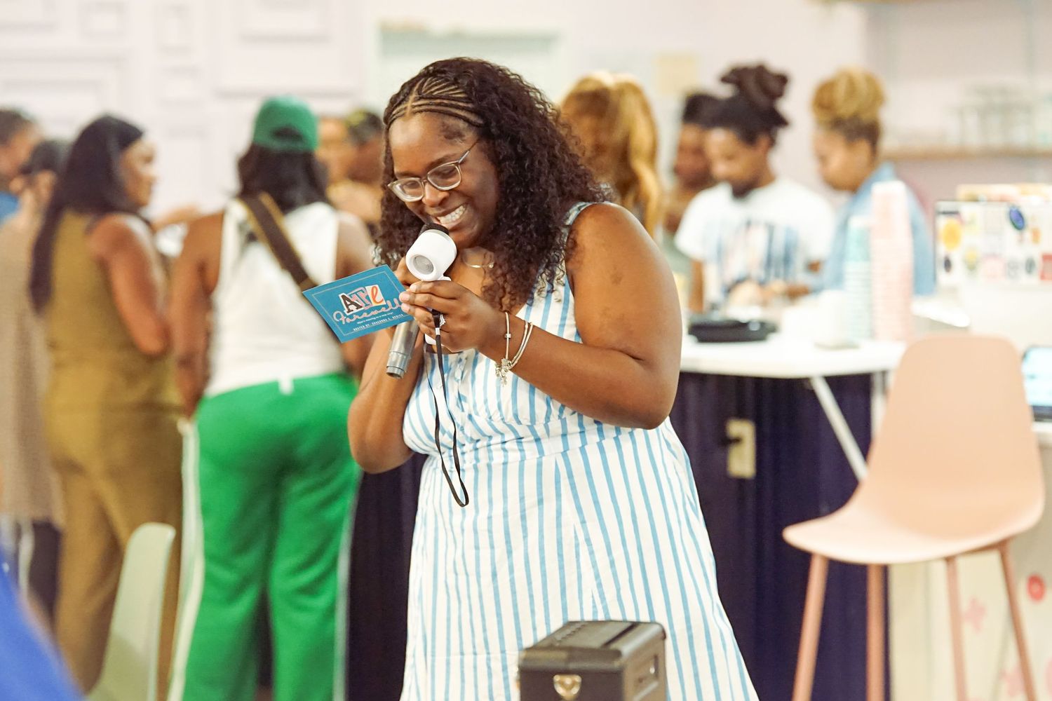 Smiling Black woman in a striped dress looking at a book during a vibrant indoor community event.