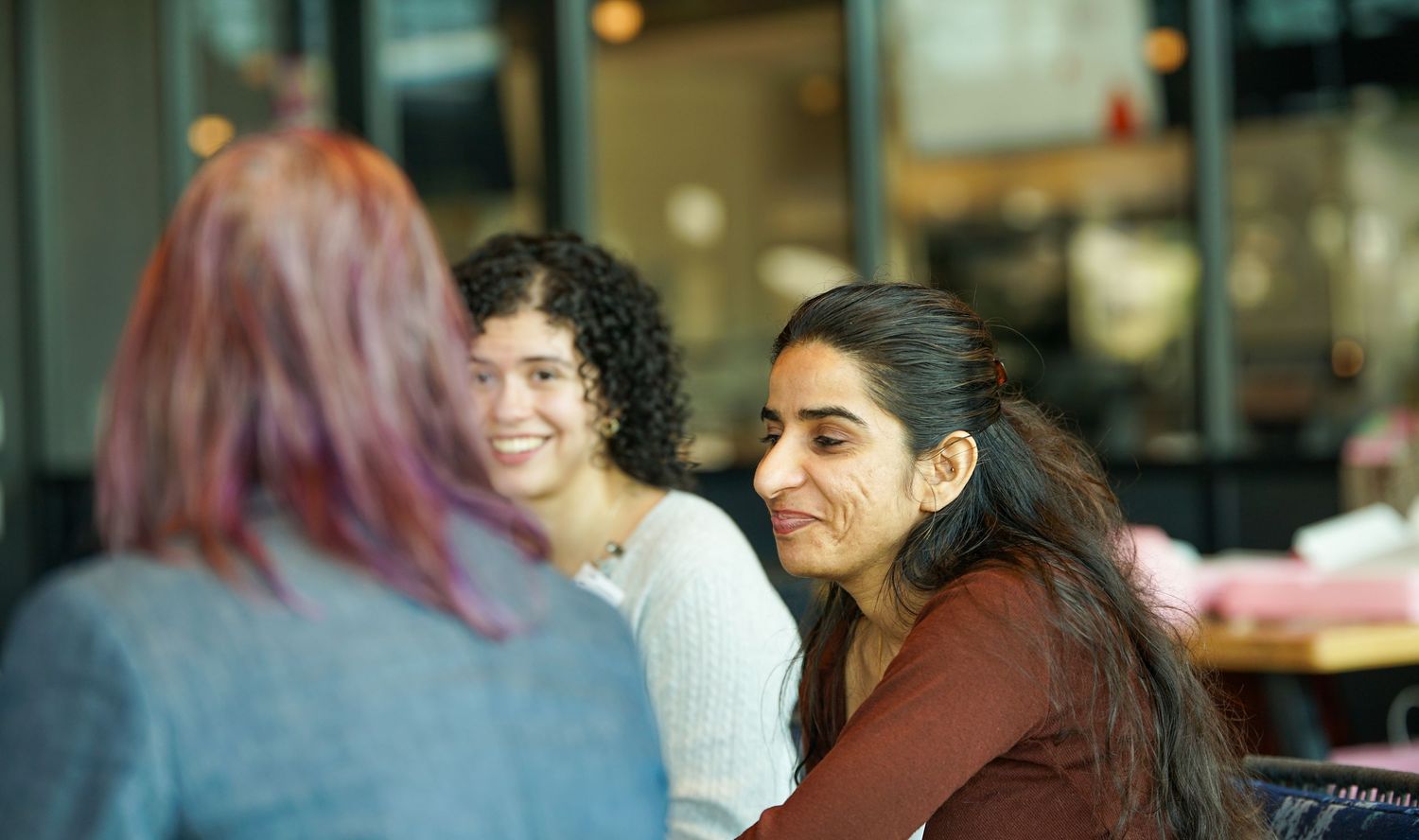 Two smiling women enjoy a conversation at a casual cafe setting.