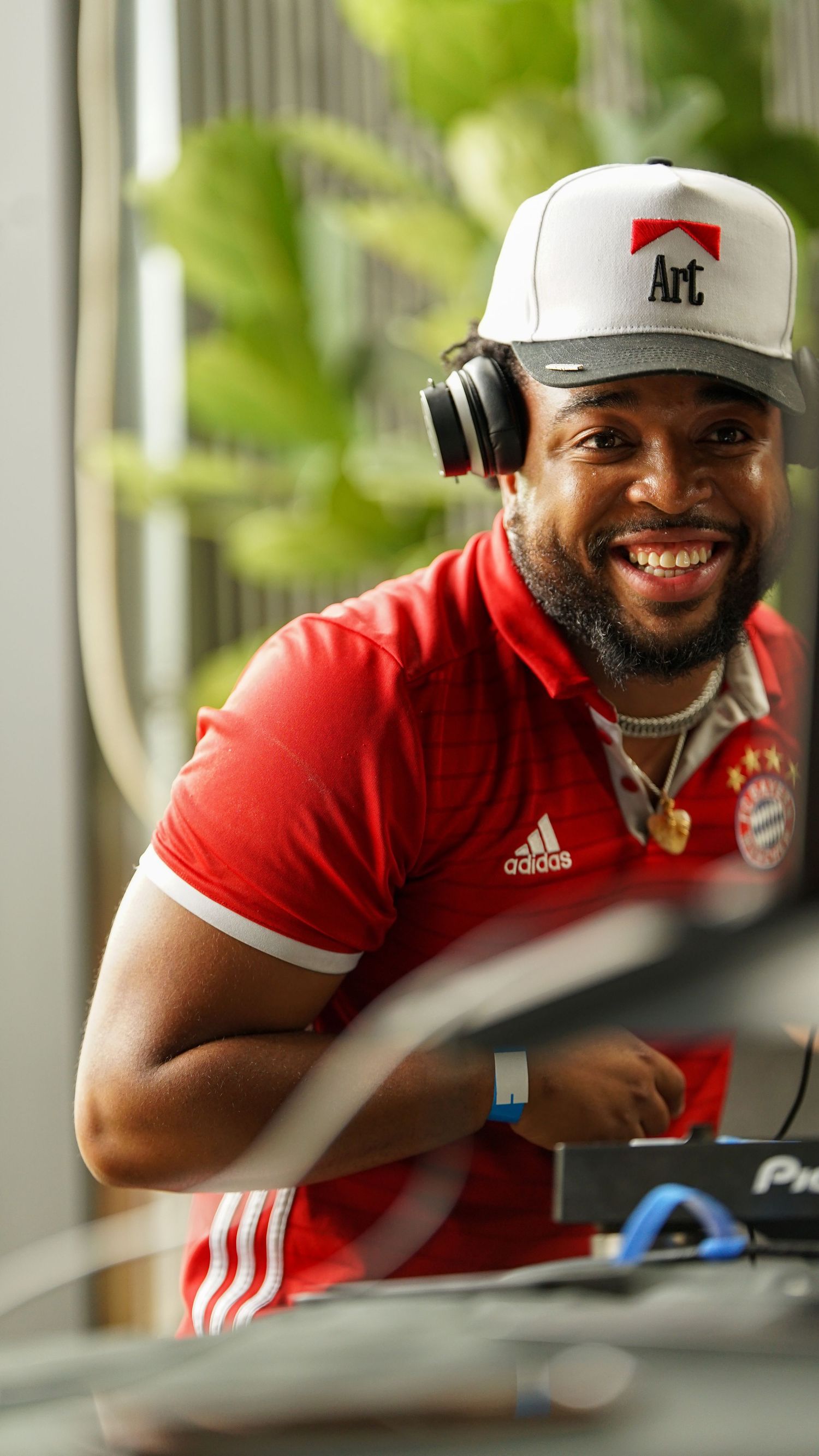 Person in red Adidas shirt and white cap smiling while sitting at a desk.
