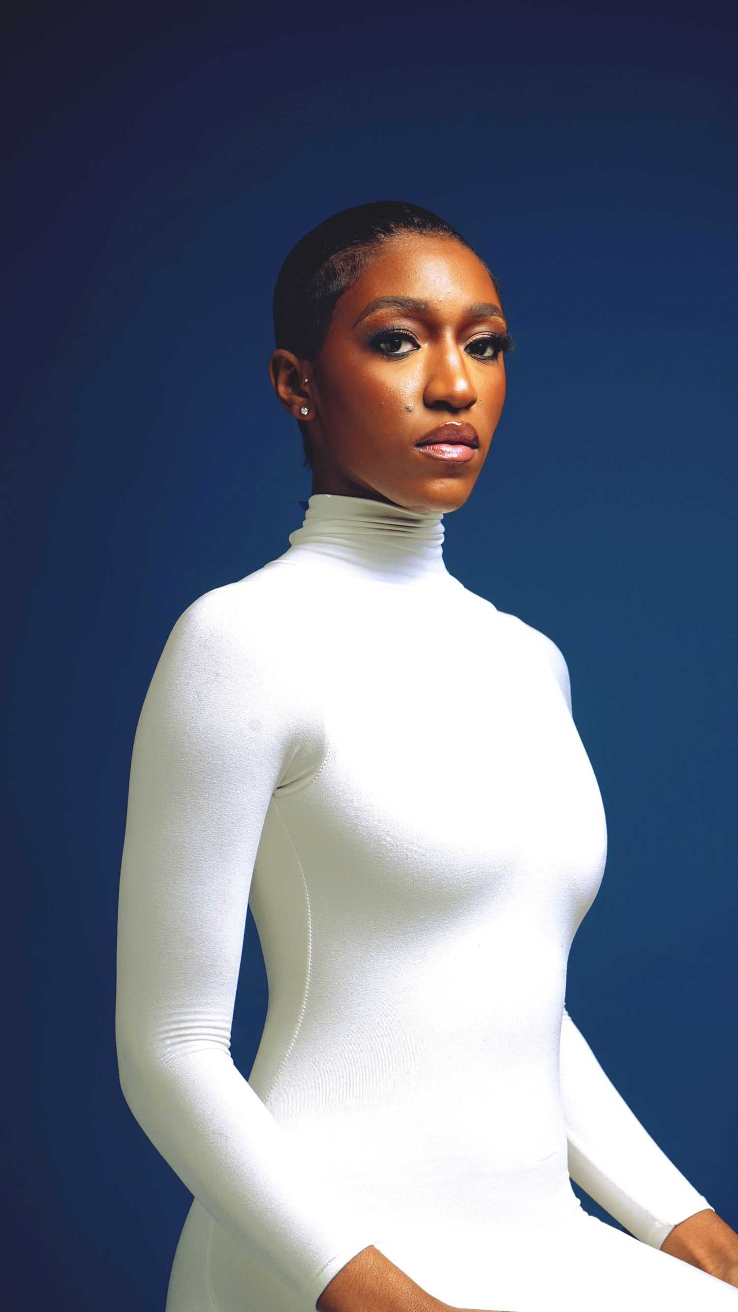 Fashion portrait in white turtleneck against deep blue studio background.