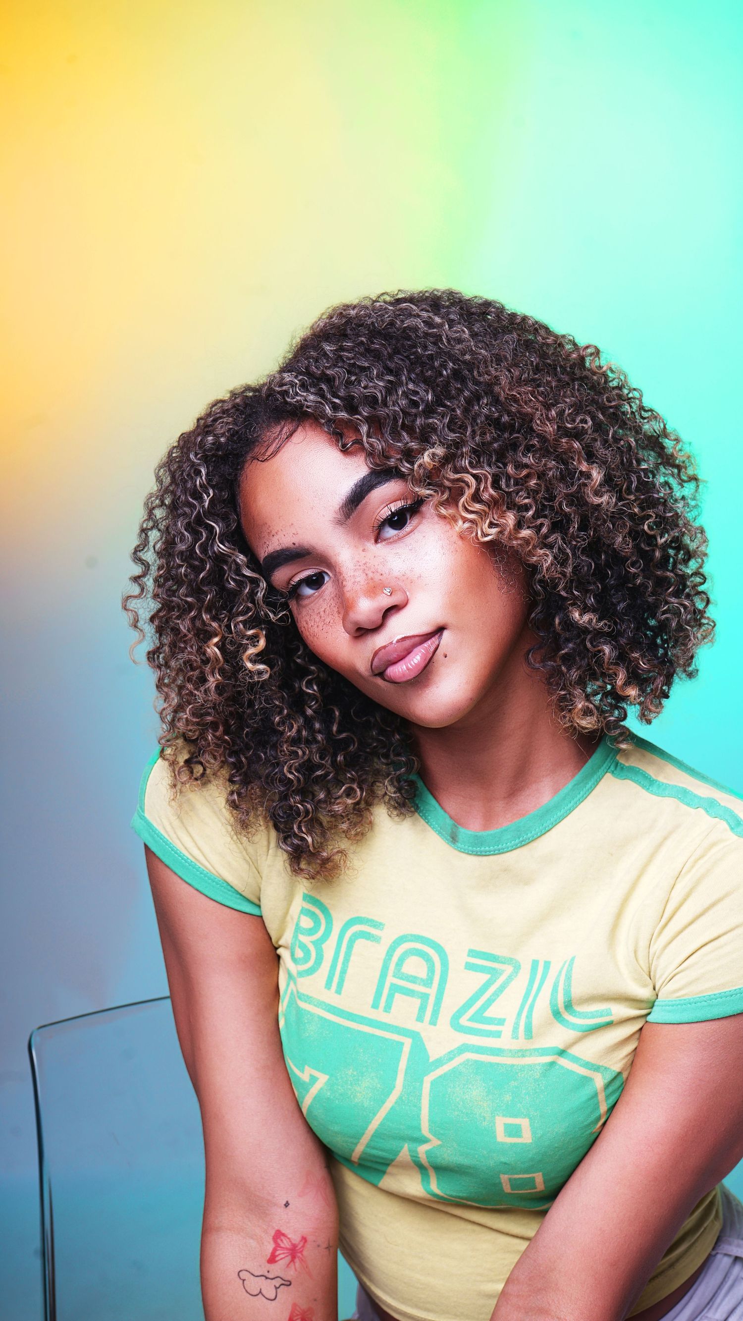 Playful poses in yellow and mint green retro-style t-shirt against colorful gradient backdrop.