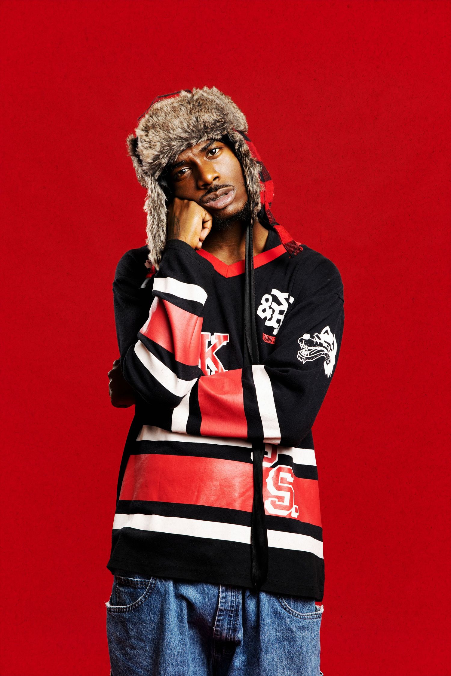 Fashion model wearing a black and red color block sweater with fur trim hood against a red background.