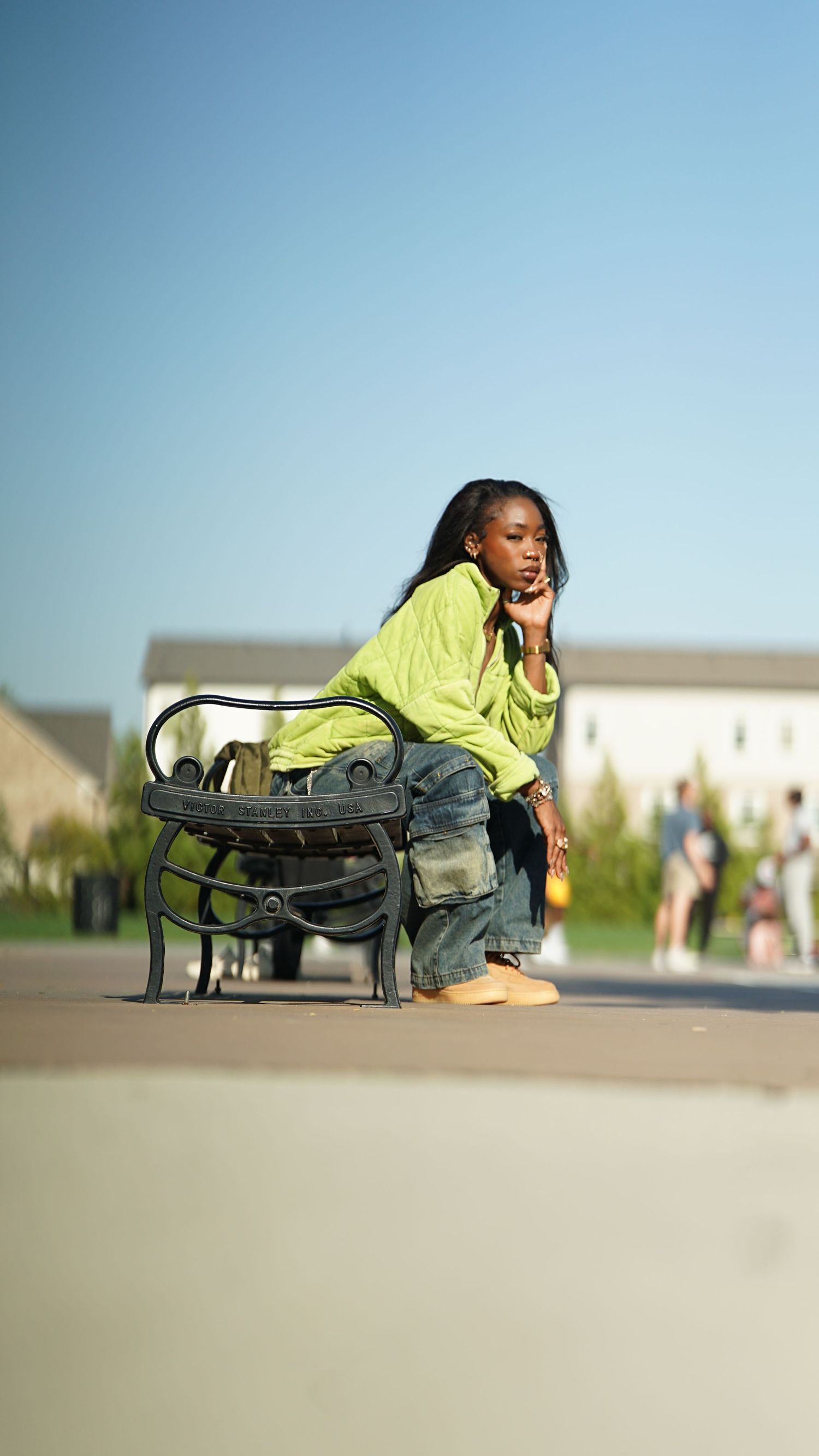 Person in neon yellow jacket and jeans sits thoughtfully on outdoor bench during golden hour.