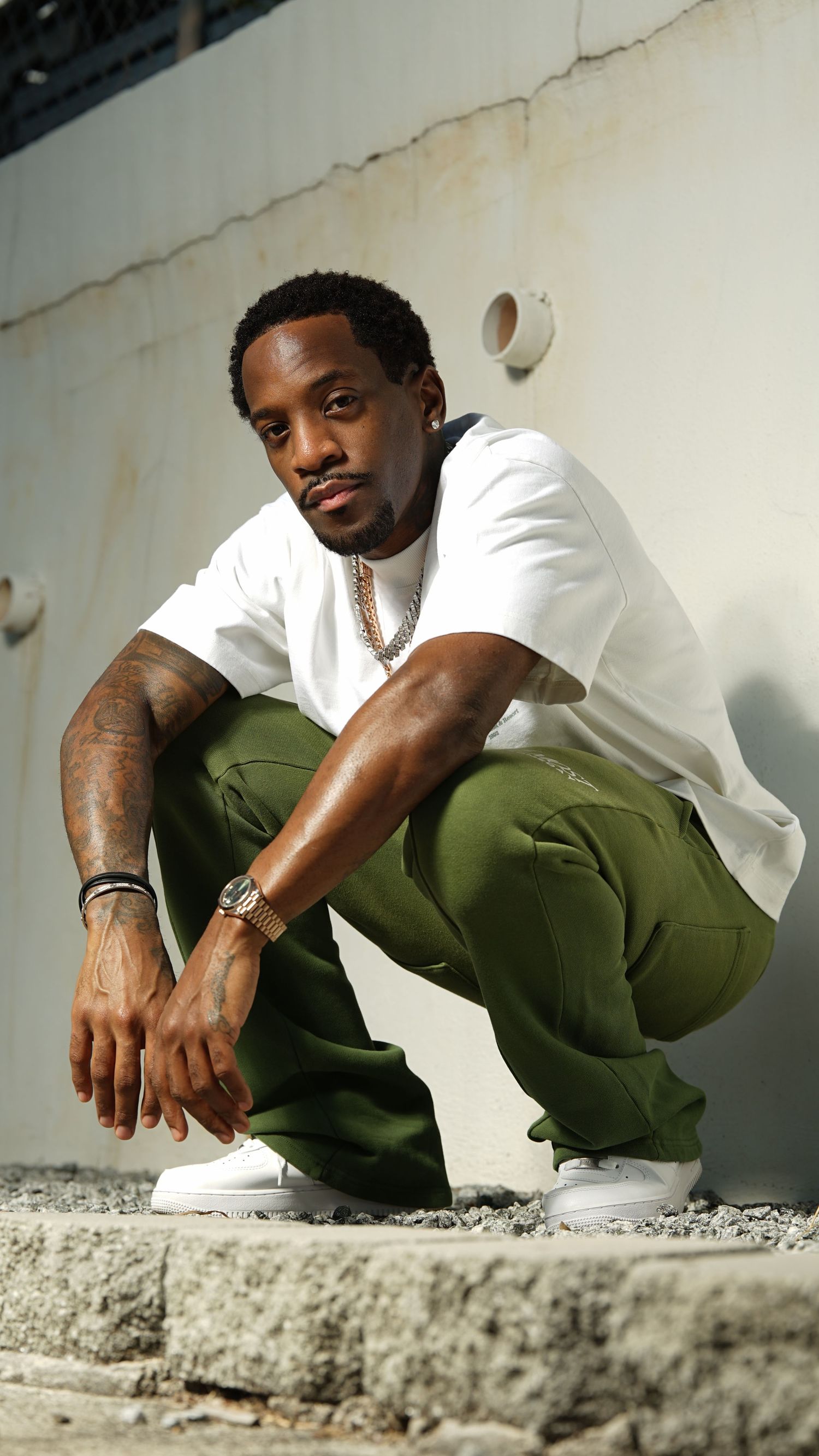 Person in olive cargo pants and white shirt sits casually on concrete ledge in urban setting.