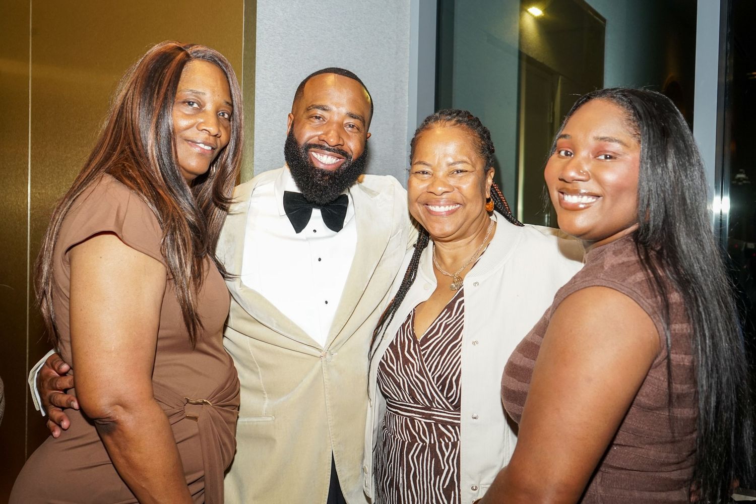 Four people smiling and posing together at a formal event, man in white tuxedo with bow tie.
