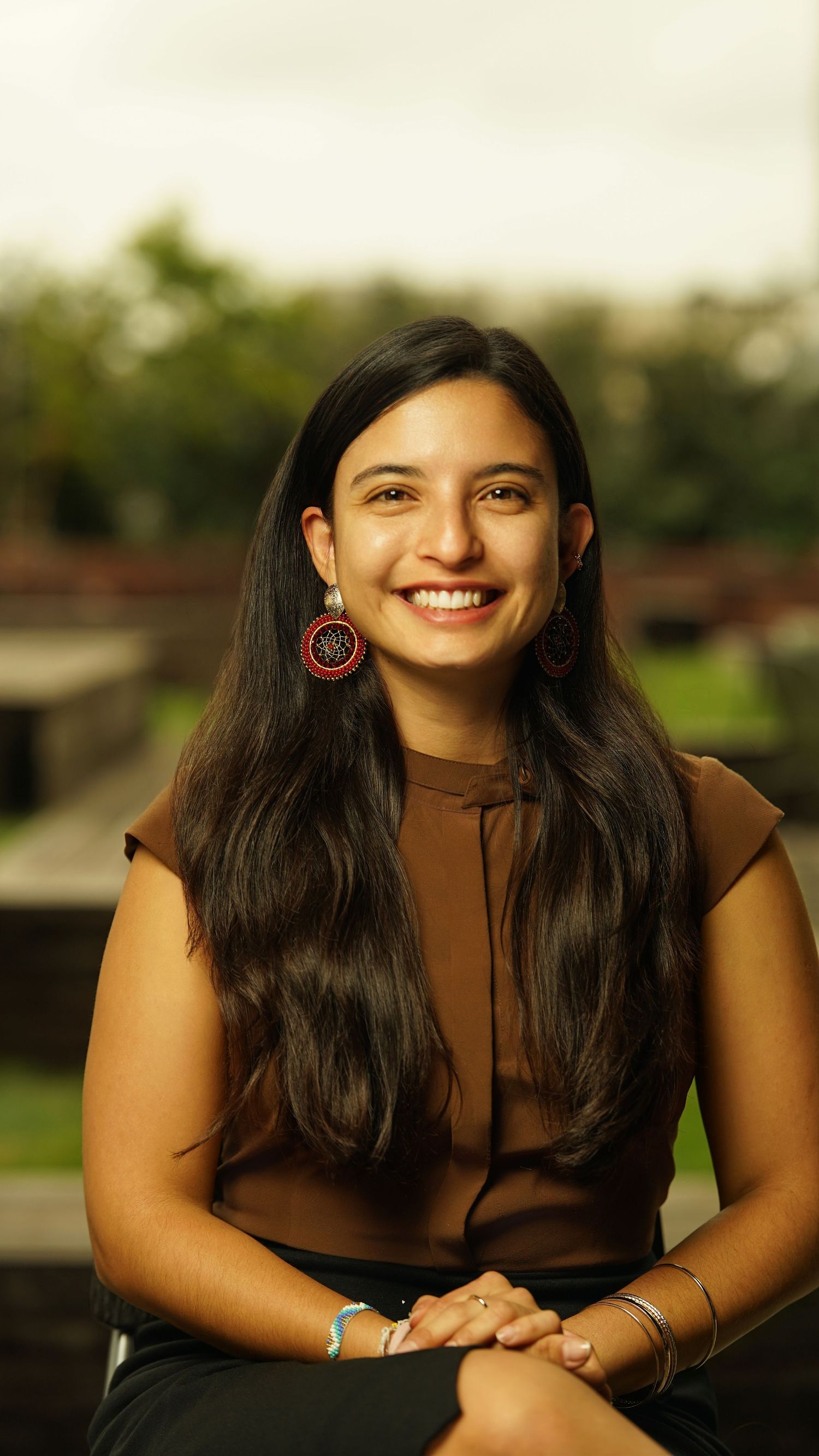 Casual portrait of person in dark top with long dark hair smiling brightly outdoors.
