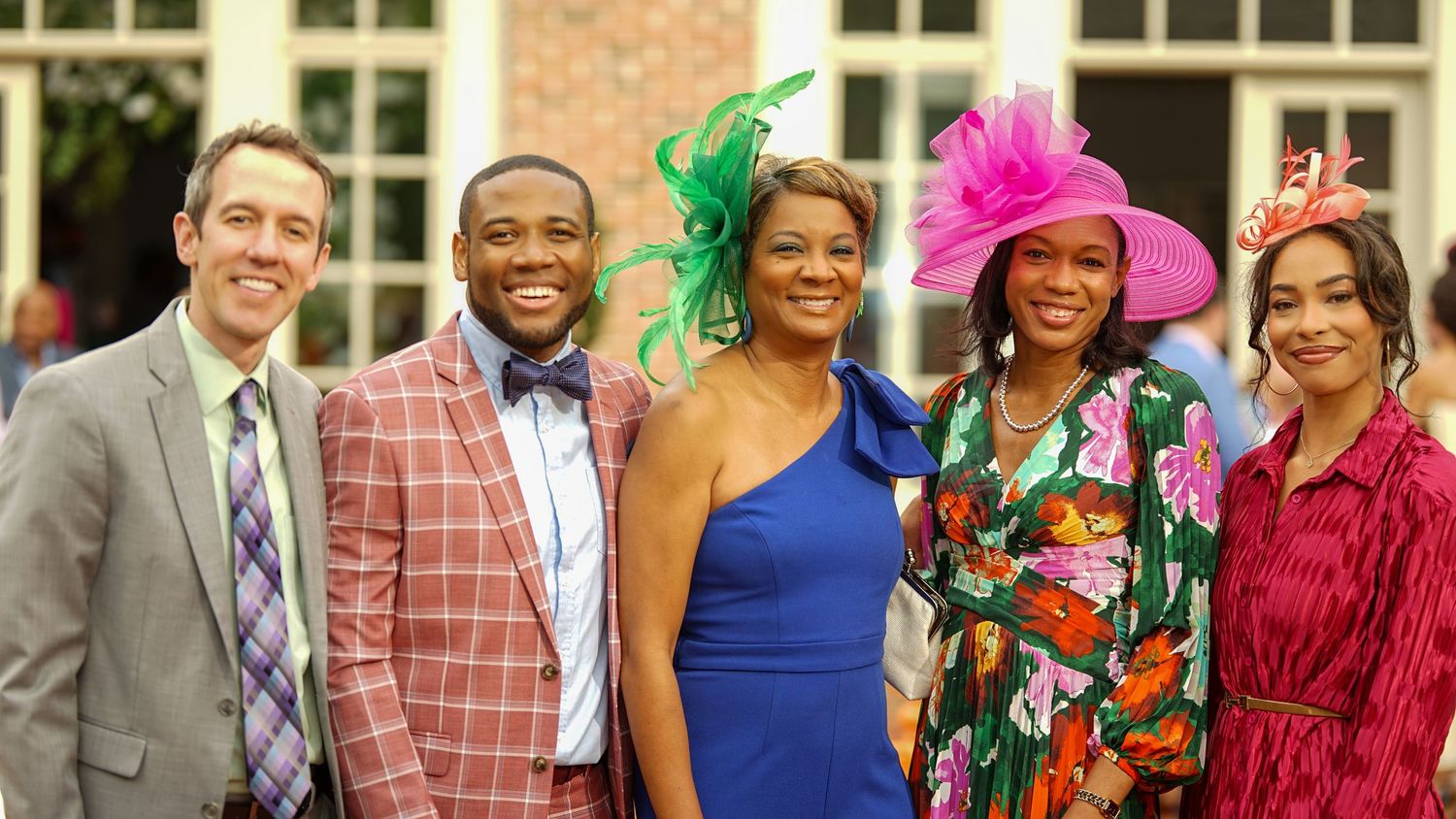 Group photo of well-dressed party guests wearing colorful outfits and fancy hats at formal event.