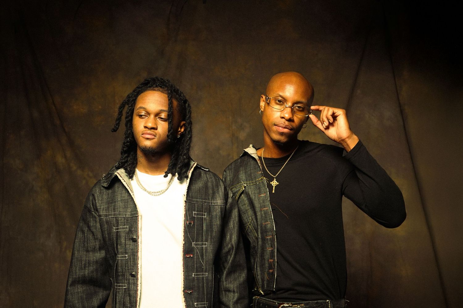 Two musicians pose against a dark textured background wearing casual urban attire.