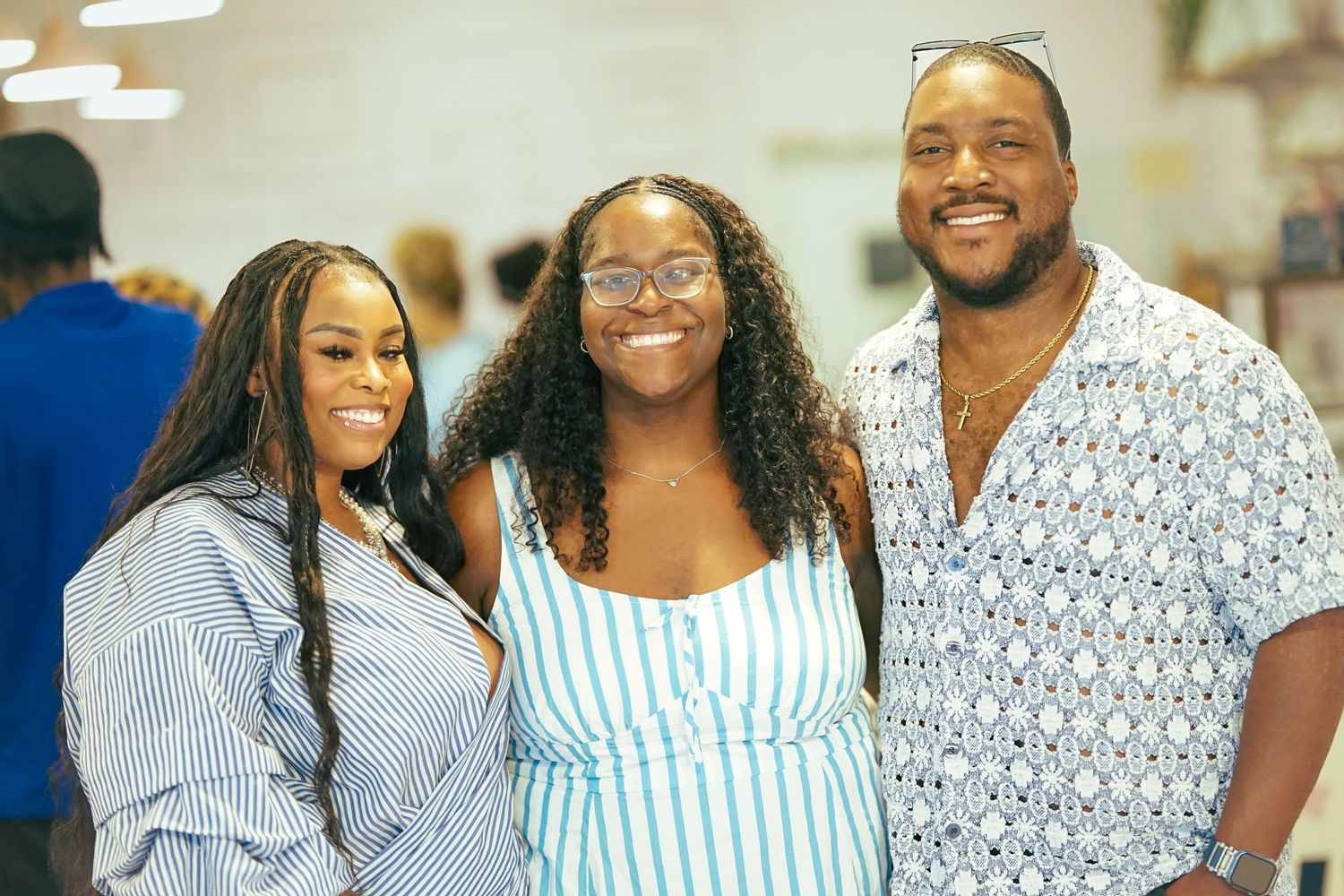 Three smiling friends posing together at an indoor event, wearing casual summer outfits in blue and white tones.