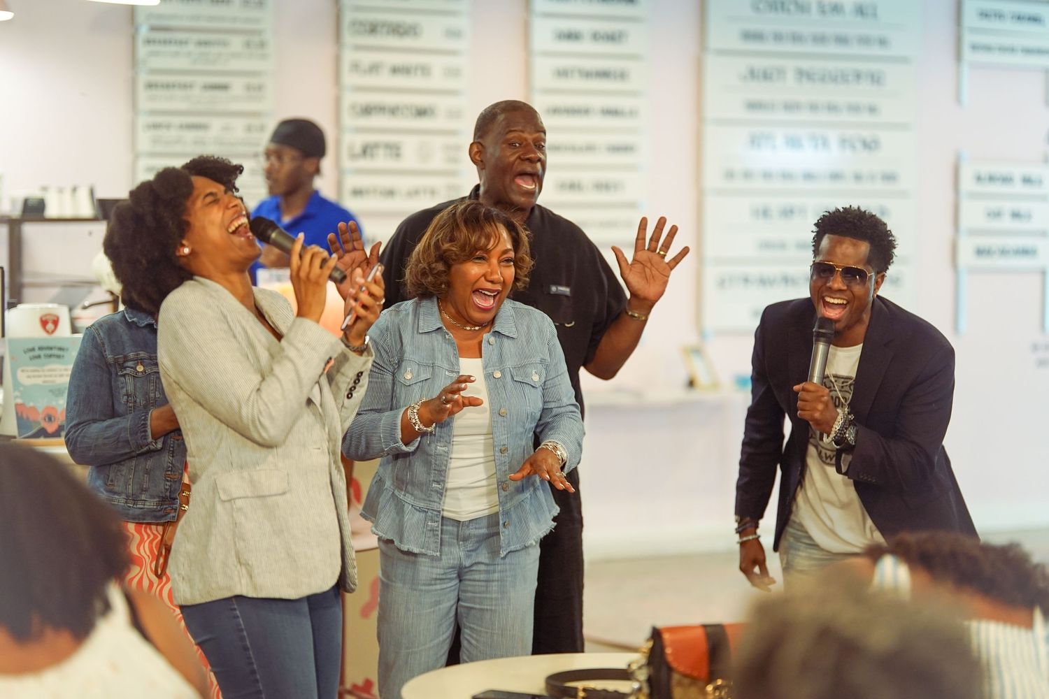 Group of joyful Black people laughing and celebrating together inside a modern cafe or event space.
