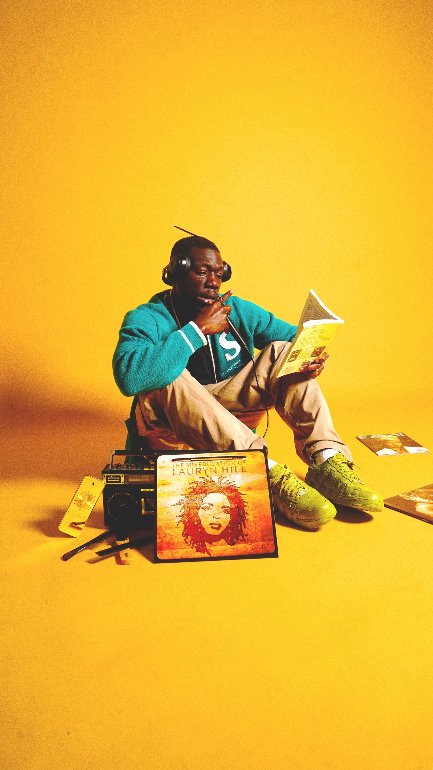 Person in teal sweater reads book against vibrant yellow backdrop.