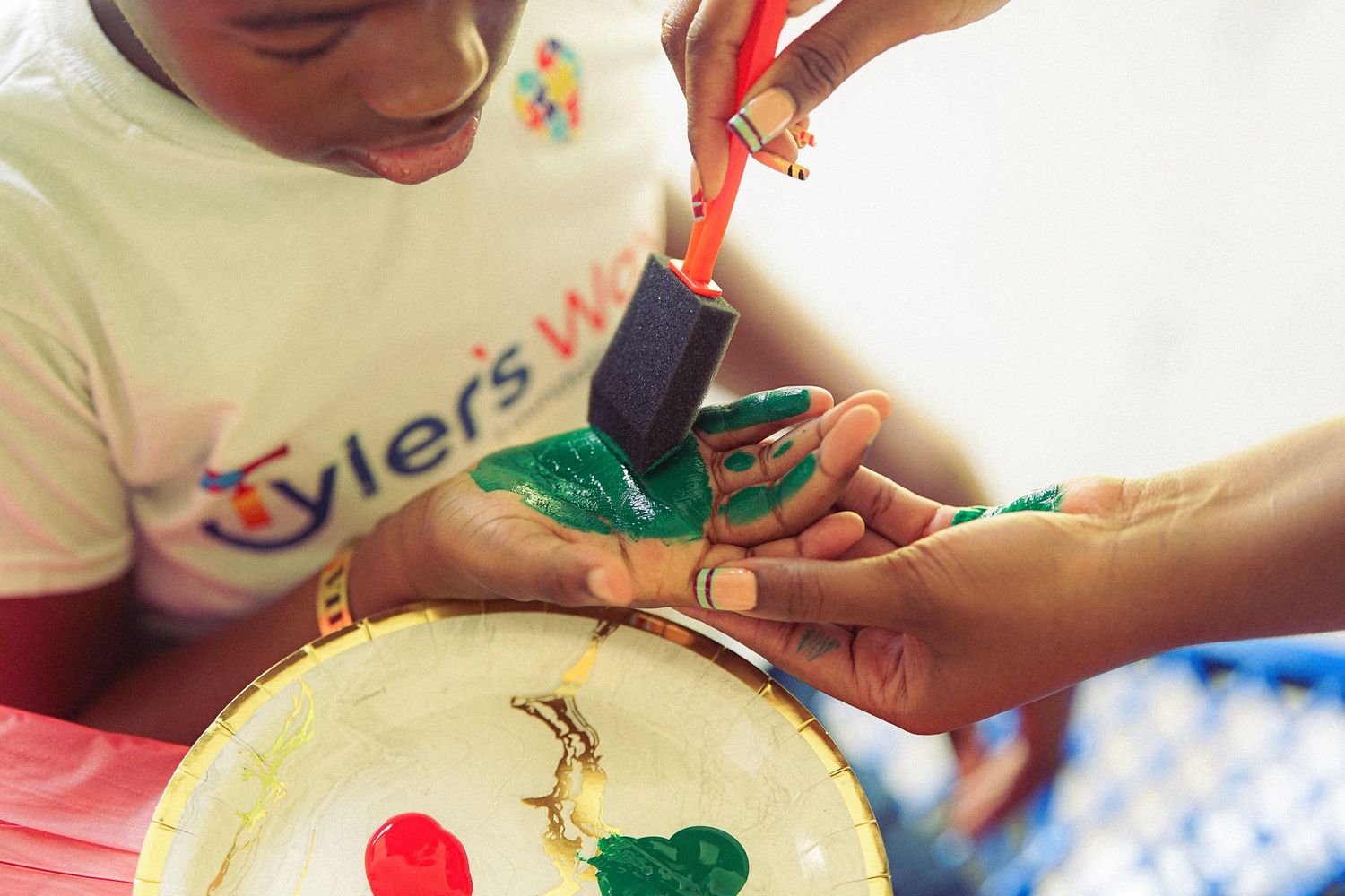 Child painting a colorful plate with a foam brush at Tyler's World art activity.