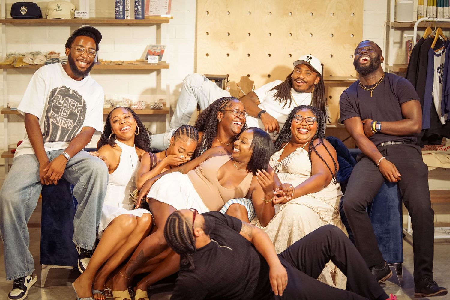 A diverse group of young Black friends laughing and posing together in a cozy boutique shop setting.