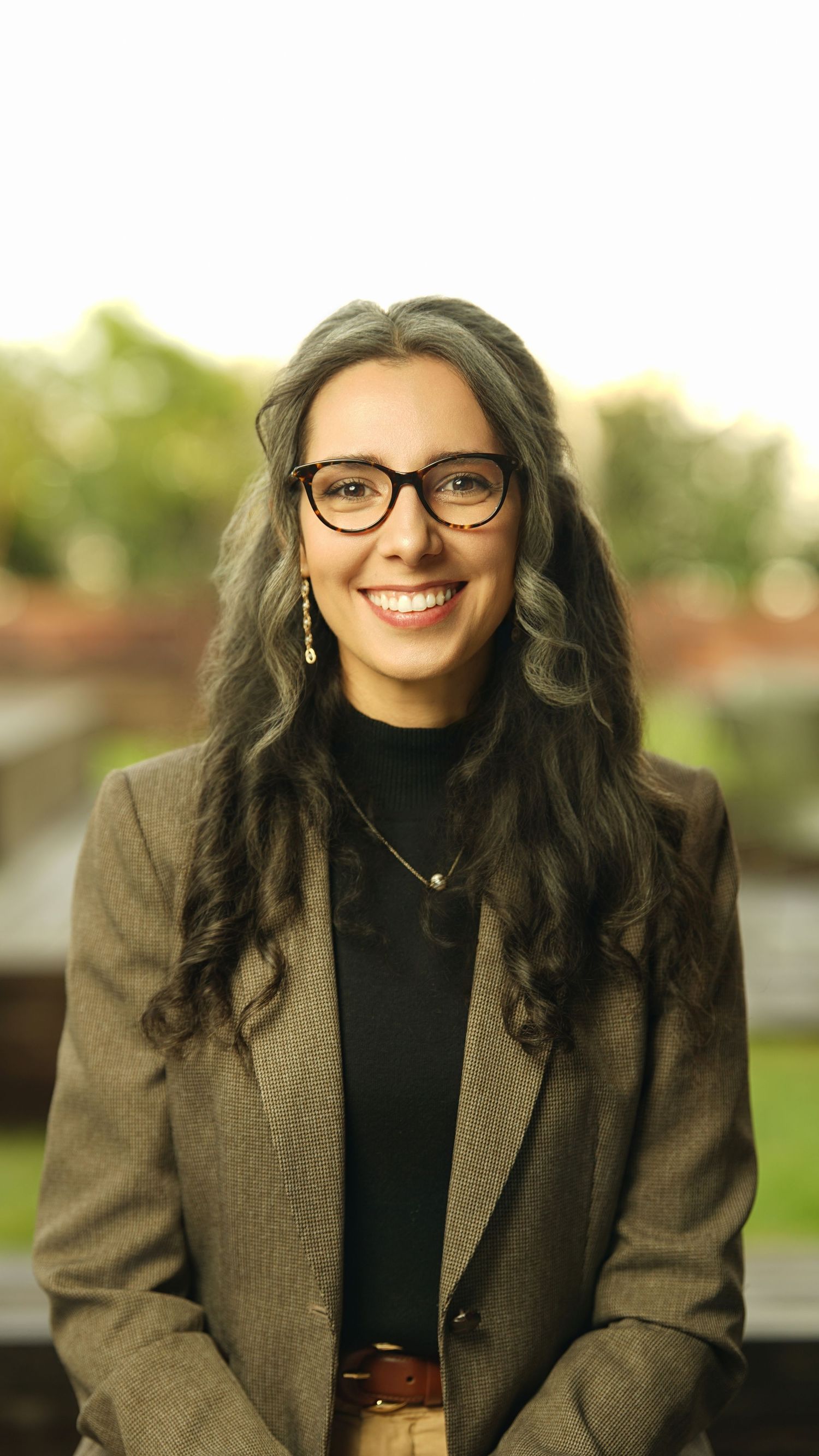 Professional headshots of someone in glasses and a brown blazer with long wavy hair.
