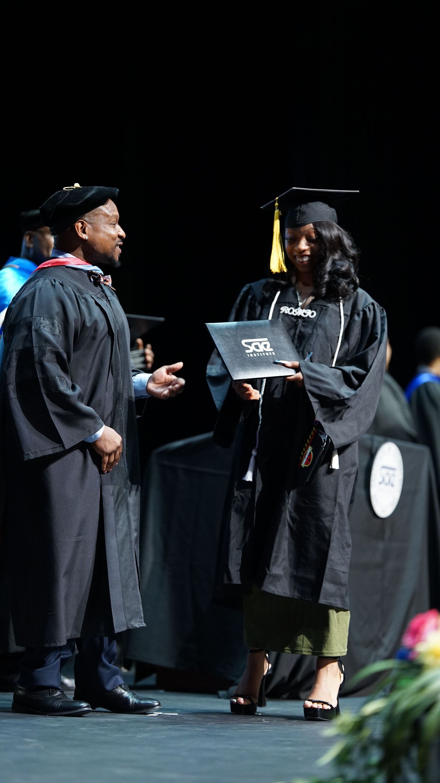 Graduates in black caps and gowns line up on stage during commencement exercises.