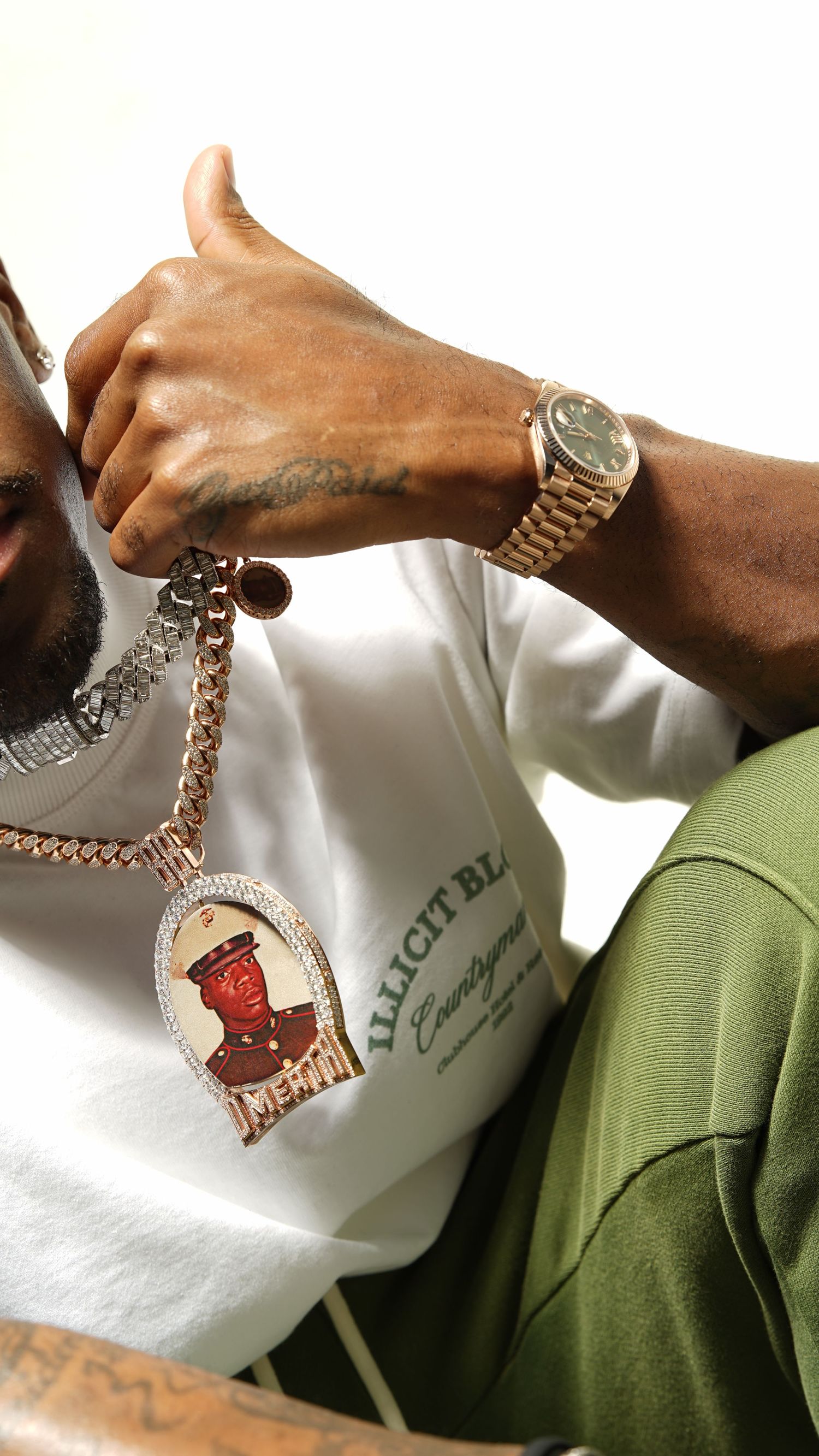 A person in a green shirt holds up a gold chain necklace with a pendant against a white background.