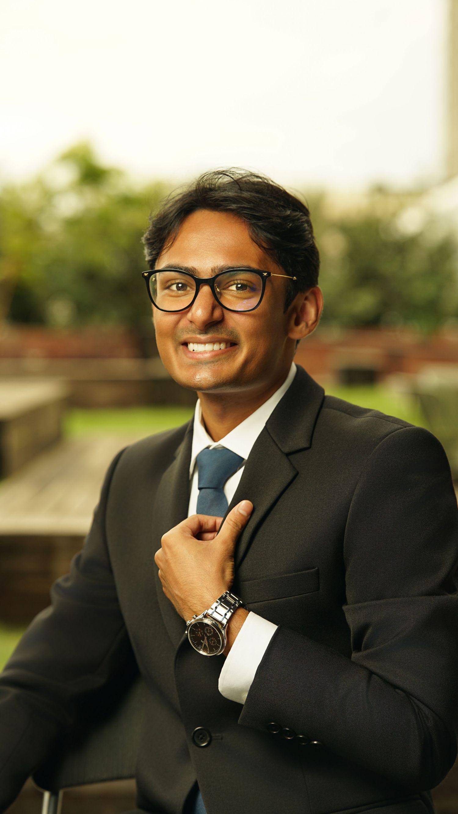 Professional in dark suit and tie adjusts collar while smiling outdoors.
