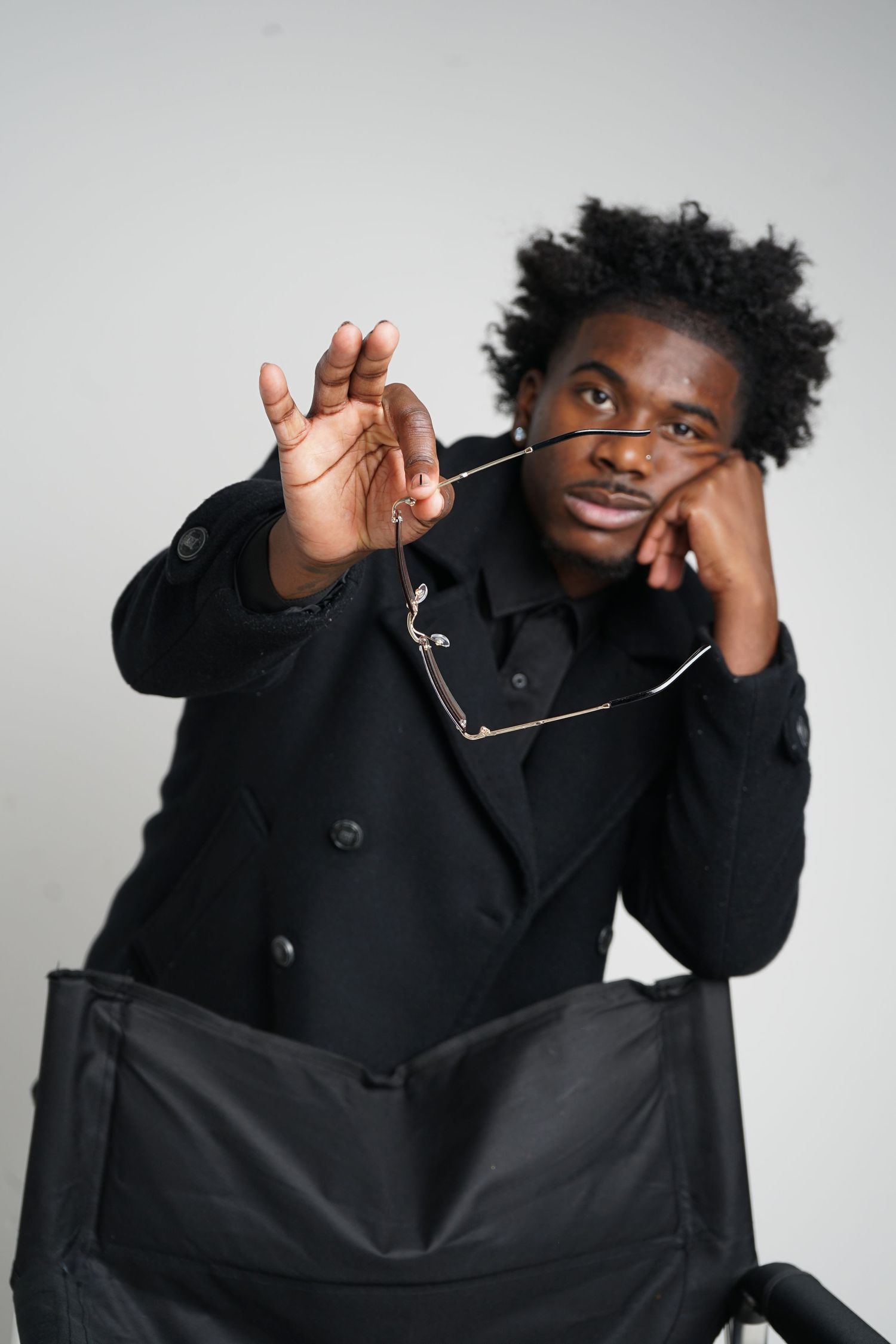Expressive portrait with model holding glasses in stylish black coat.
