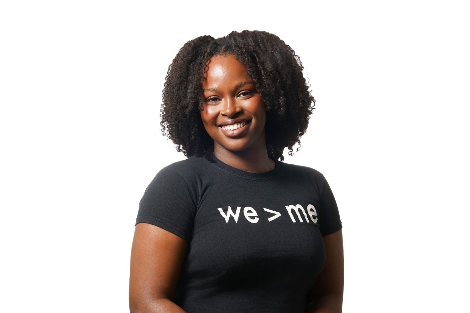 Smiling young woman wearing a black t-shirt with 'we > me' slogan, posing against a white background.