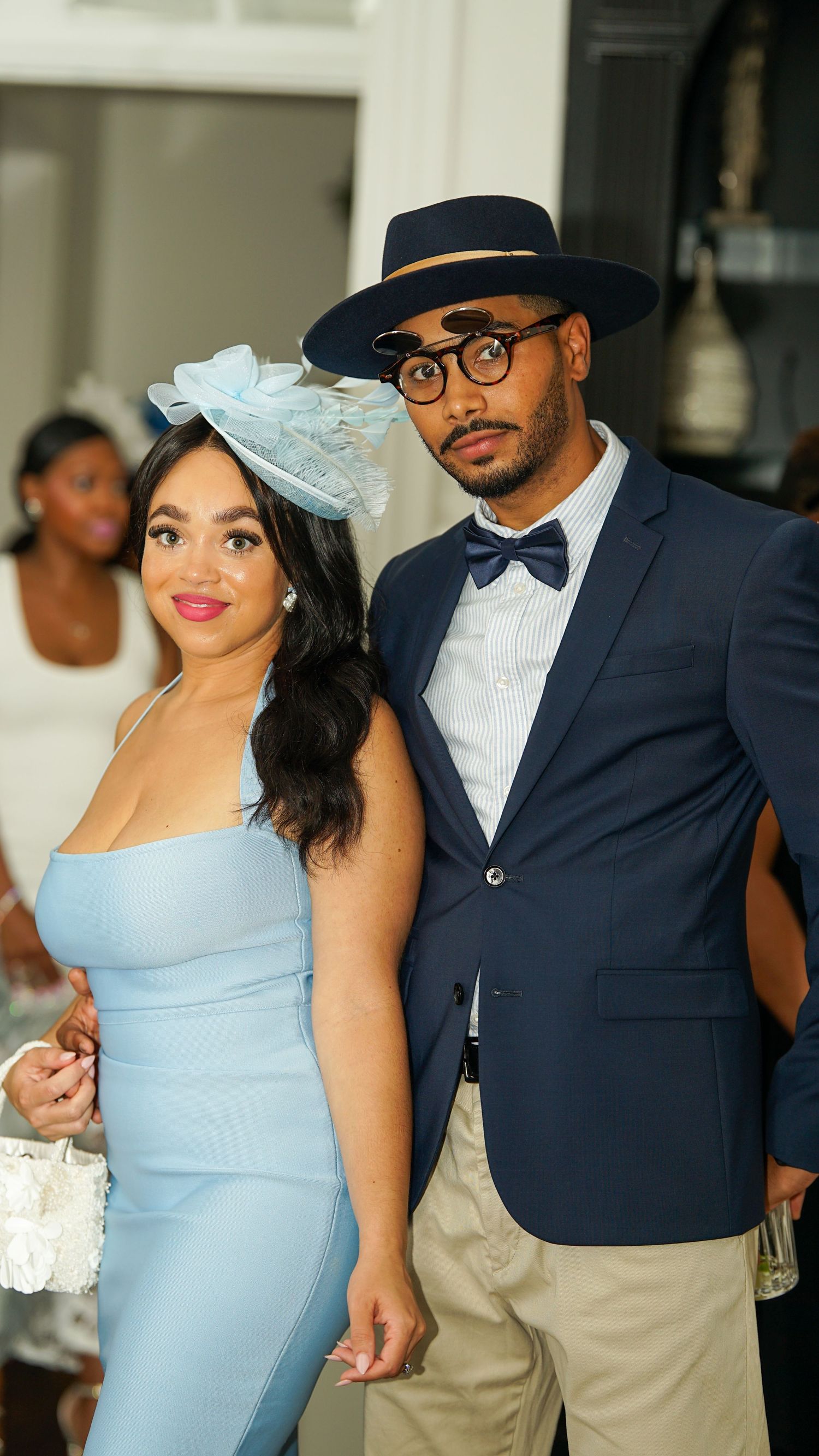 A couple dressed in formal attire with a light blue dress and navy blazer pose together at an elegant event.