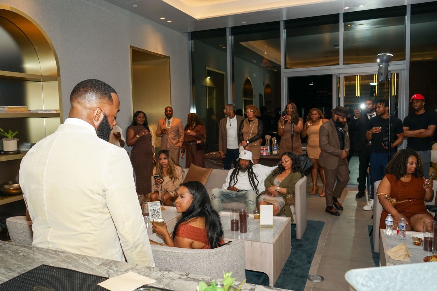 A man addresses a diverse group of guests at an elegant indoor gathering or private event.