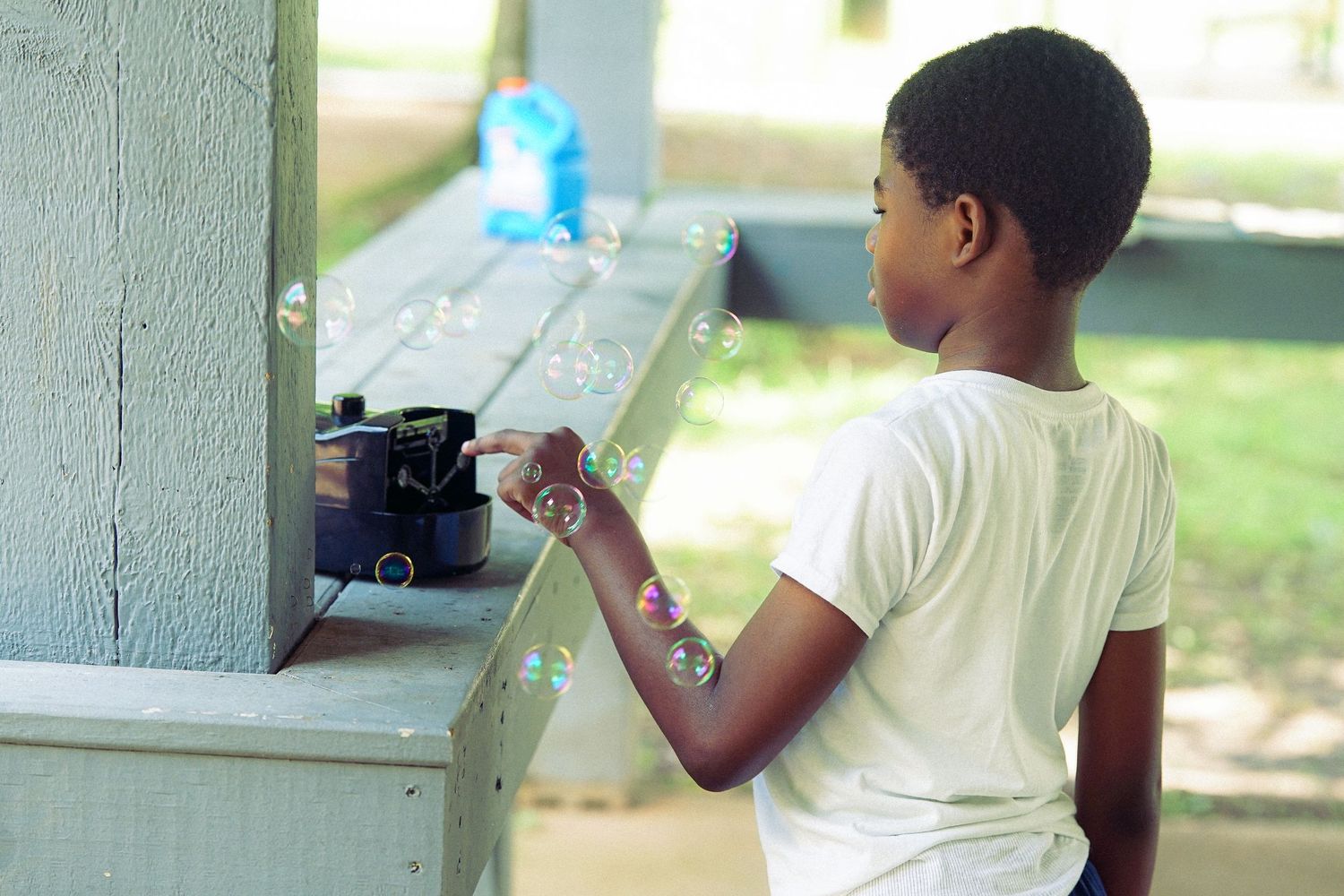 Child plays with bubble machine at outdoor community event in park setting.