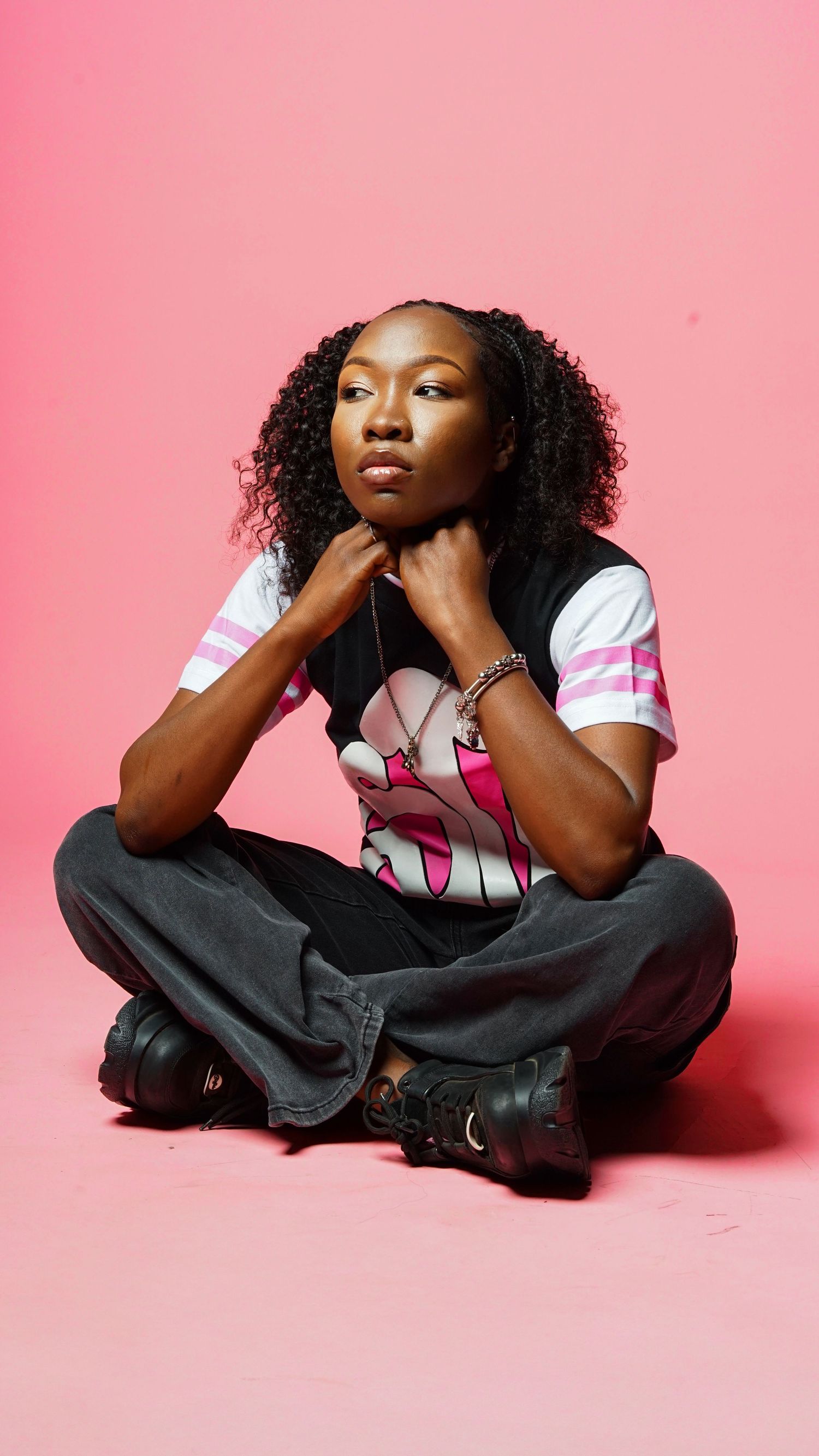Fashion model poses against pink backdrop wearing white top and dark pants in artistic portrait series.