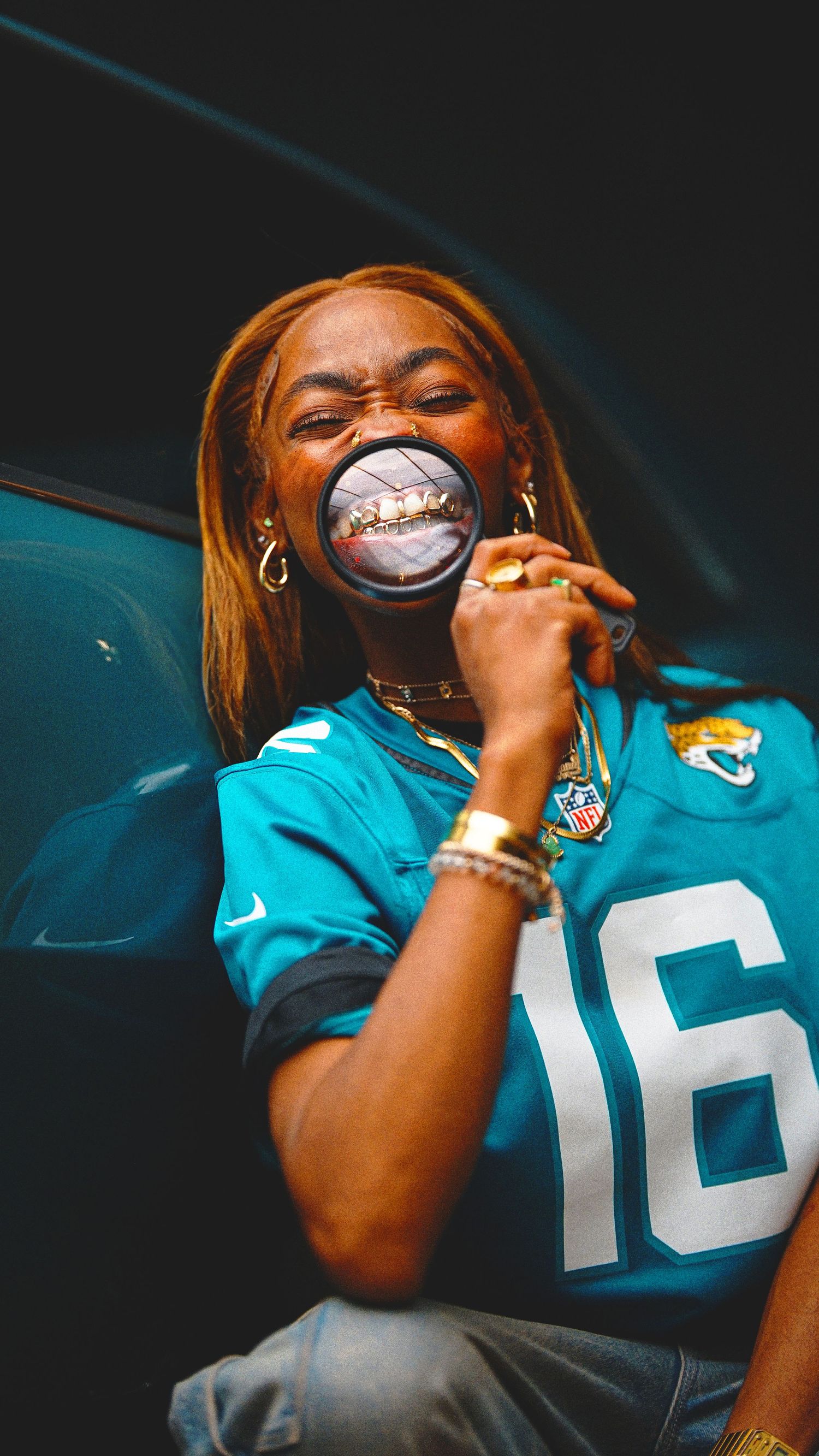 Person wearing a turquoise sports jersey performs on stage with dramatic lighting.