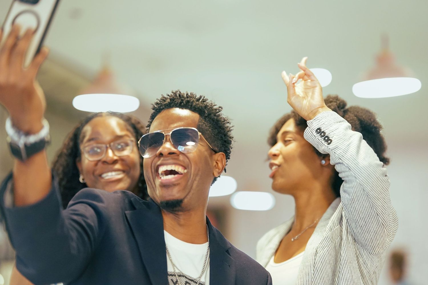 Three friends laughing and taking a selfie together in a bright indoor setting.