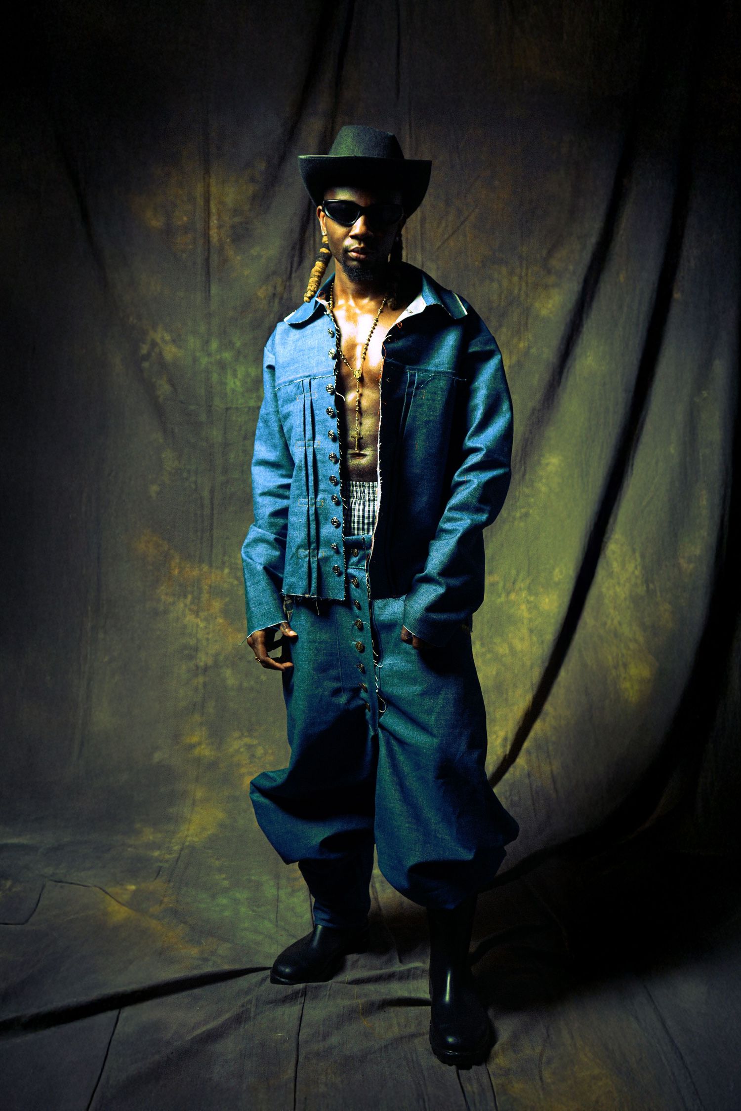 A figure in a blue blazer and black hat poses dramatically against a dark background in a series of moody shots.