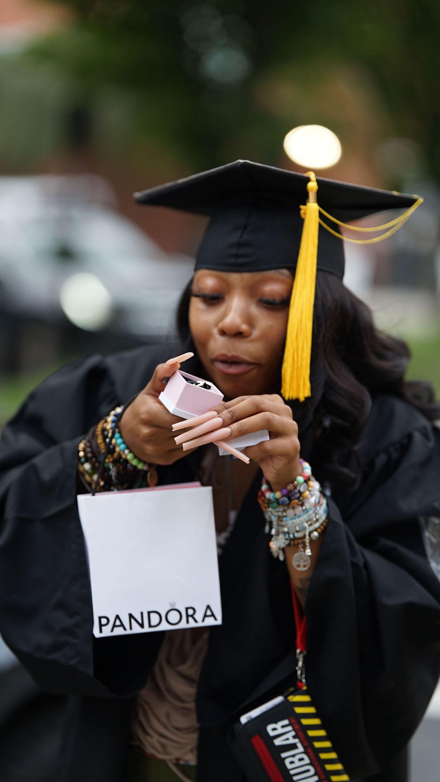 Graduate in academic regalia opens Pandora envelope during ceremony.