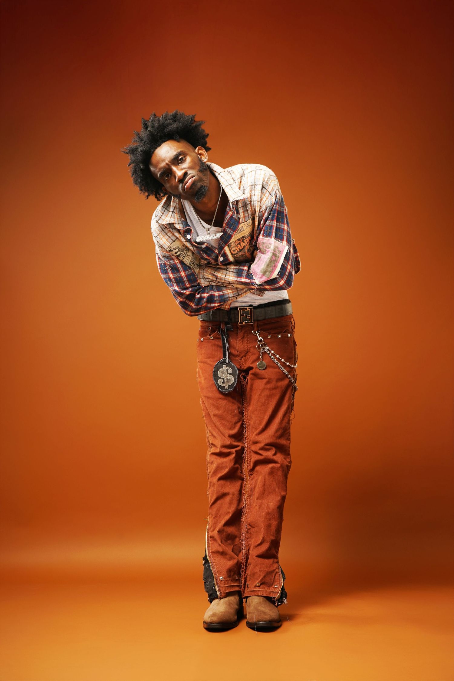 Playful bent-over pose in casual streetwear against warm orange studio background.
