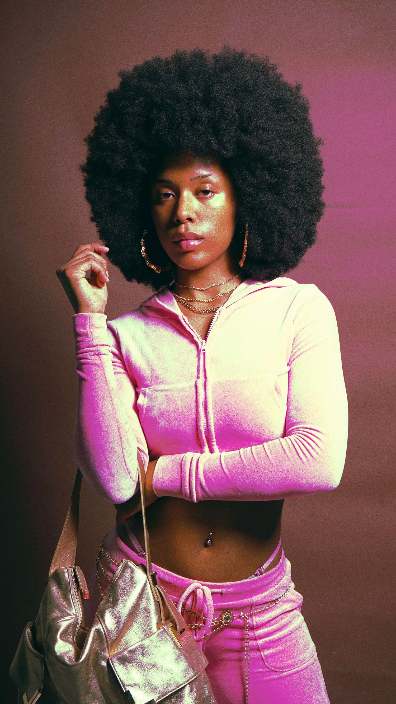Model in pink tracksuit and afro hairstyle poses against colorful studio backdrop.