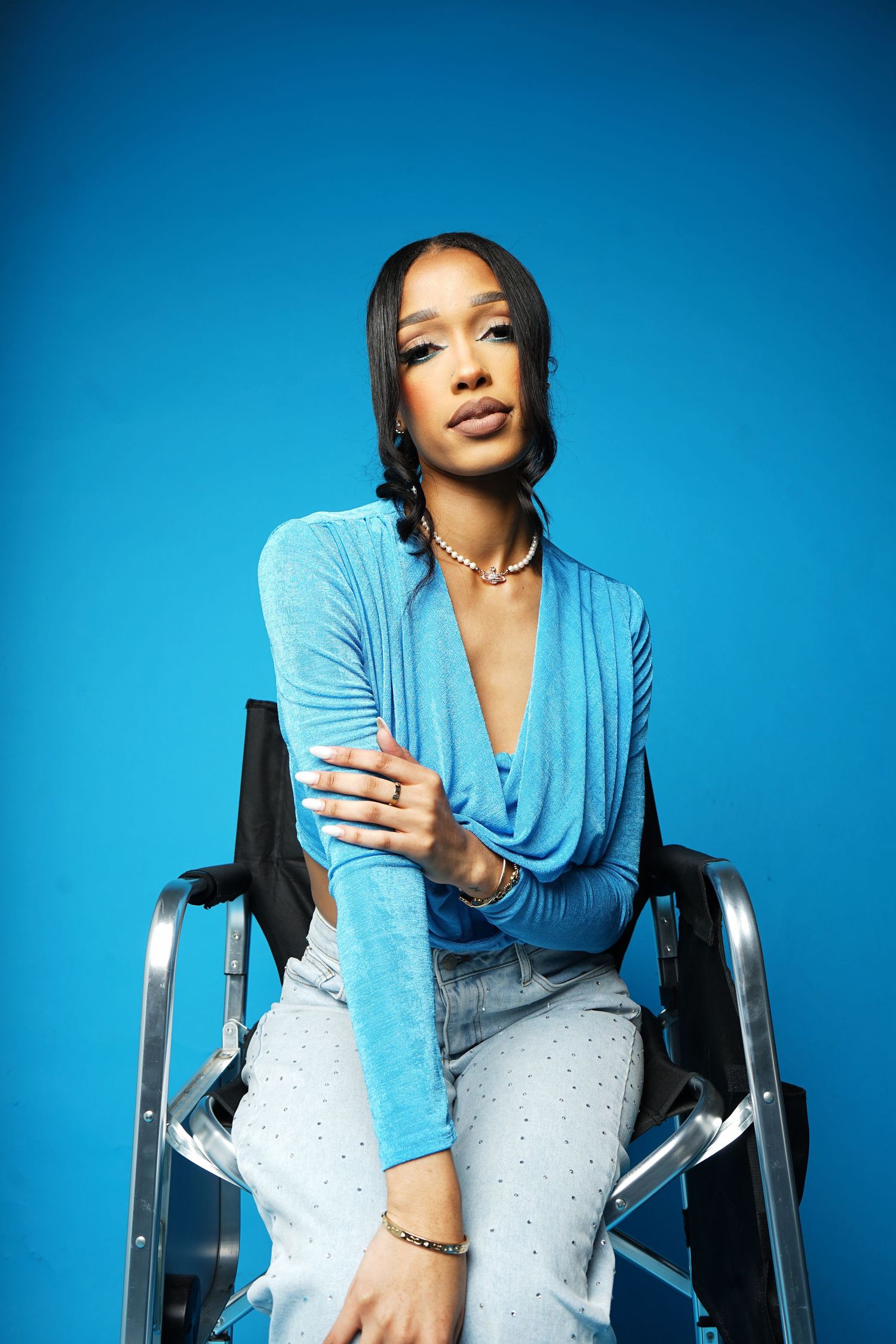 Professional photoshoot in a wheelchair against a vibrant blue background wearing a draped blue top.