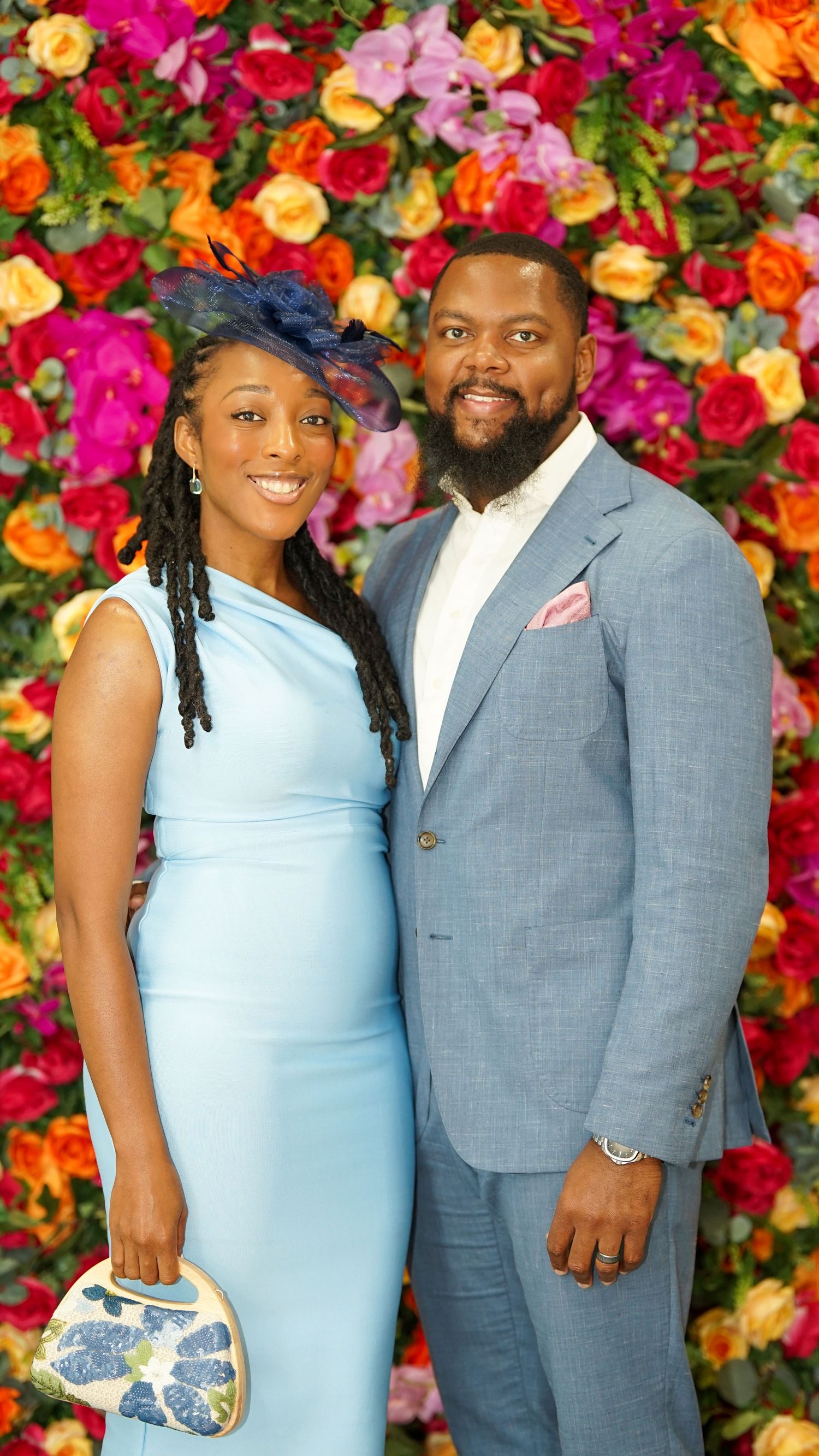 Formal event attendees in light blue and grey attire posing against colorful flower wall.