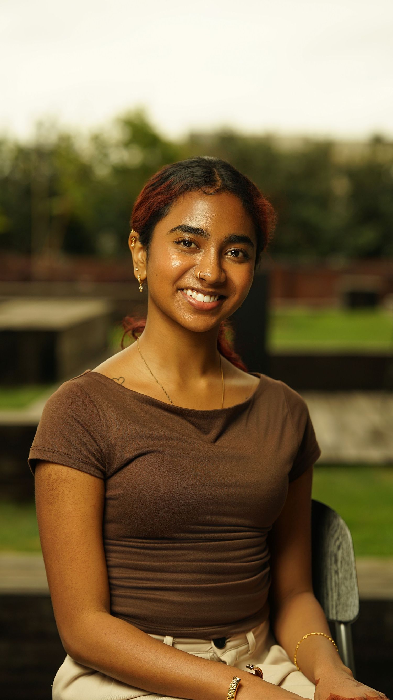 Person in brown top smiles warmly during outdoor portrait session.