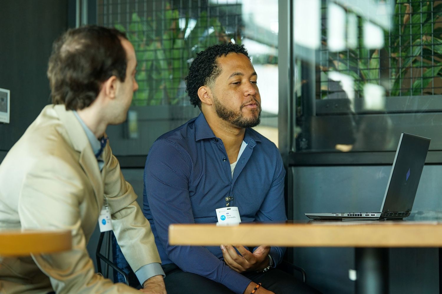 Two male colleagues having a conversation near a laptop in a modern office setting.