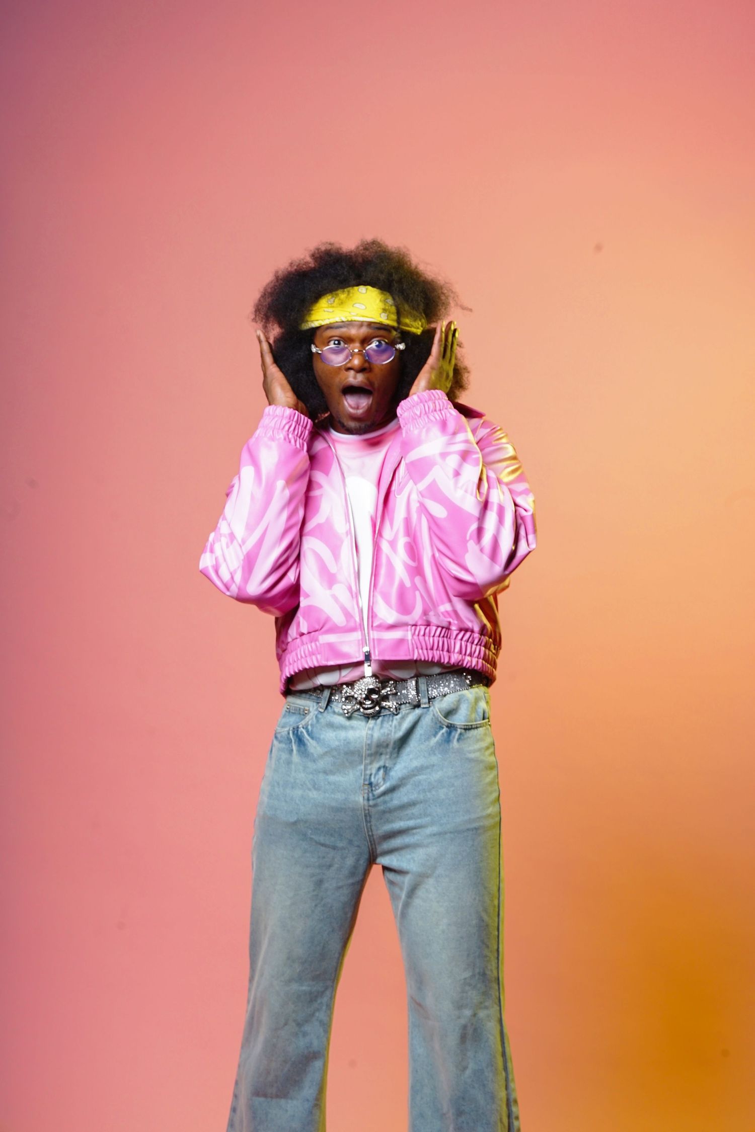 Fashion model poses in pink jacket and jeans against coral background showing casual urban style.