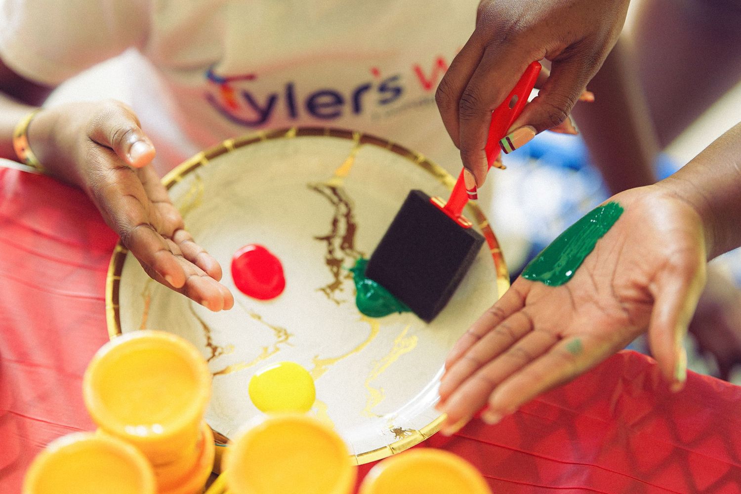 Hands with red, green, and black paint on a white palette during a creative art session.