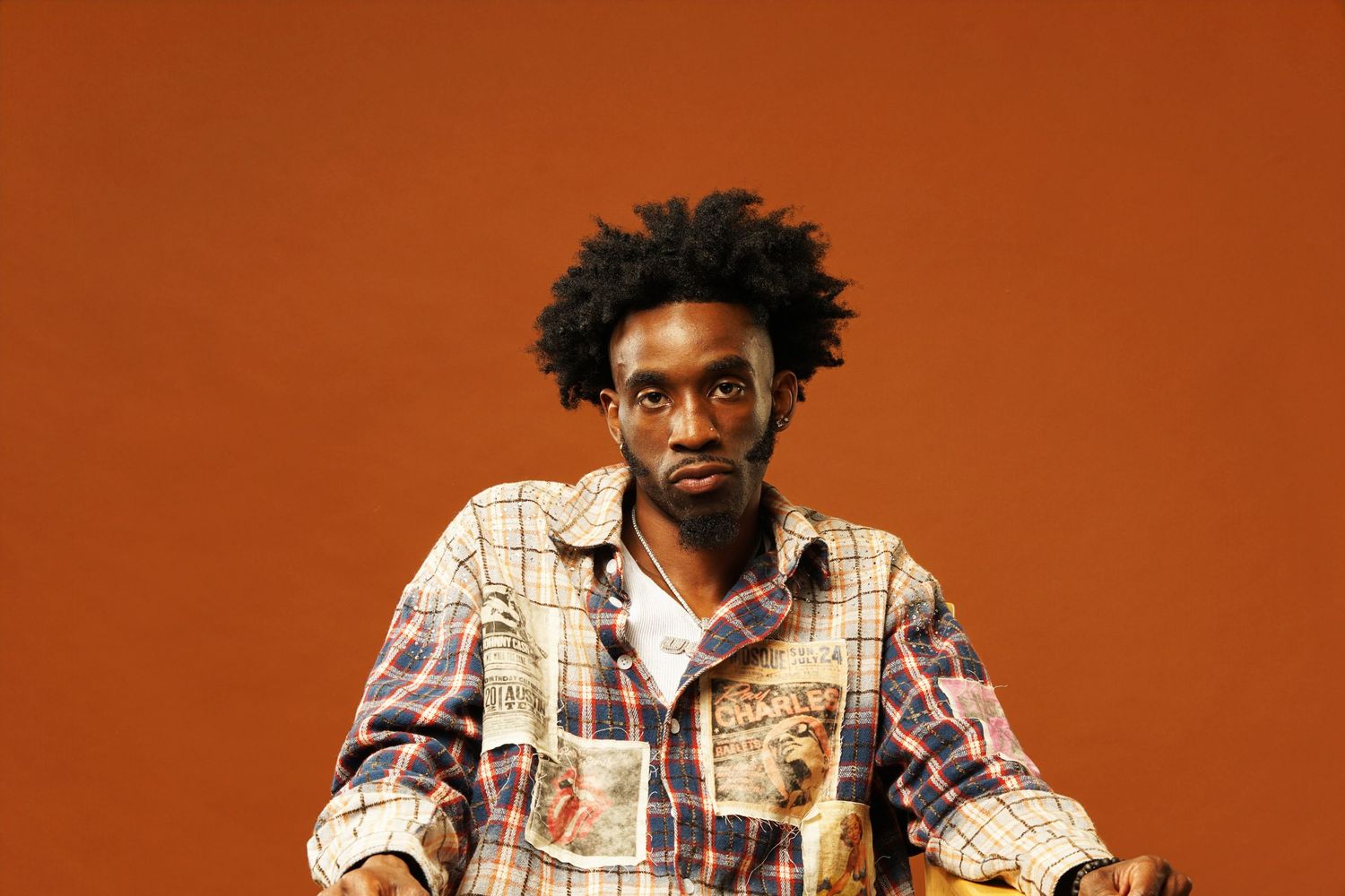 Person with glasses and plaid shirt making expressive gestures against orange background.
